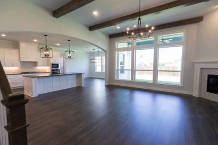 Open-concept modern living room and kitchen with dark wood flooring, white walls, large windows, a chandelier, and exposed ceiling beams. Roofing and painting in Bucks County