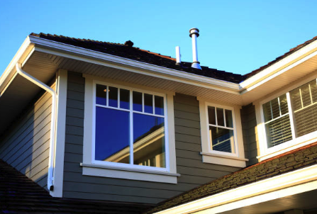Exterior view of house corner with windows and roof, in sunlight.