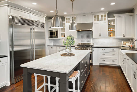 Modern kitchen with white cabinets, stainless steel appliances, large marble island, and hardwood floors.