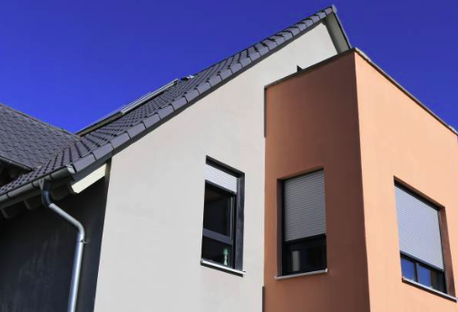 Modern house exterior with gray and orange walls, sloped roof, and closed windows under a clear blue sky. Roofing and painting in Bucks County