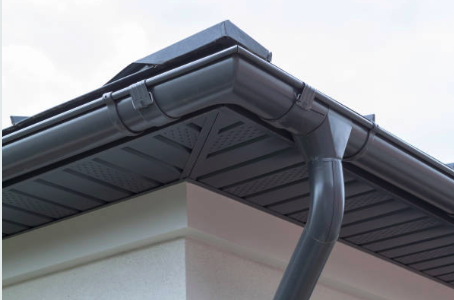 Close-up of a house roof corner with black gutters and downspout