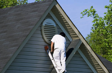 Person painting the exterior of a house on a ladder. Roofing and painting in Bucks County
