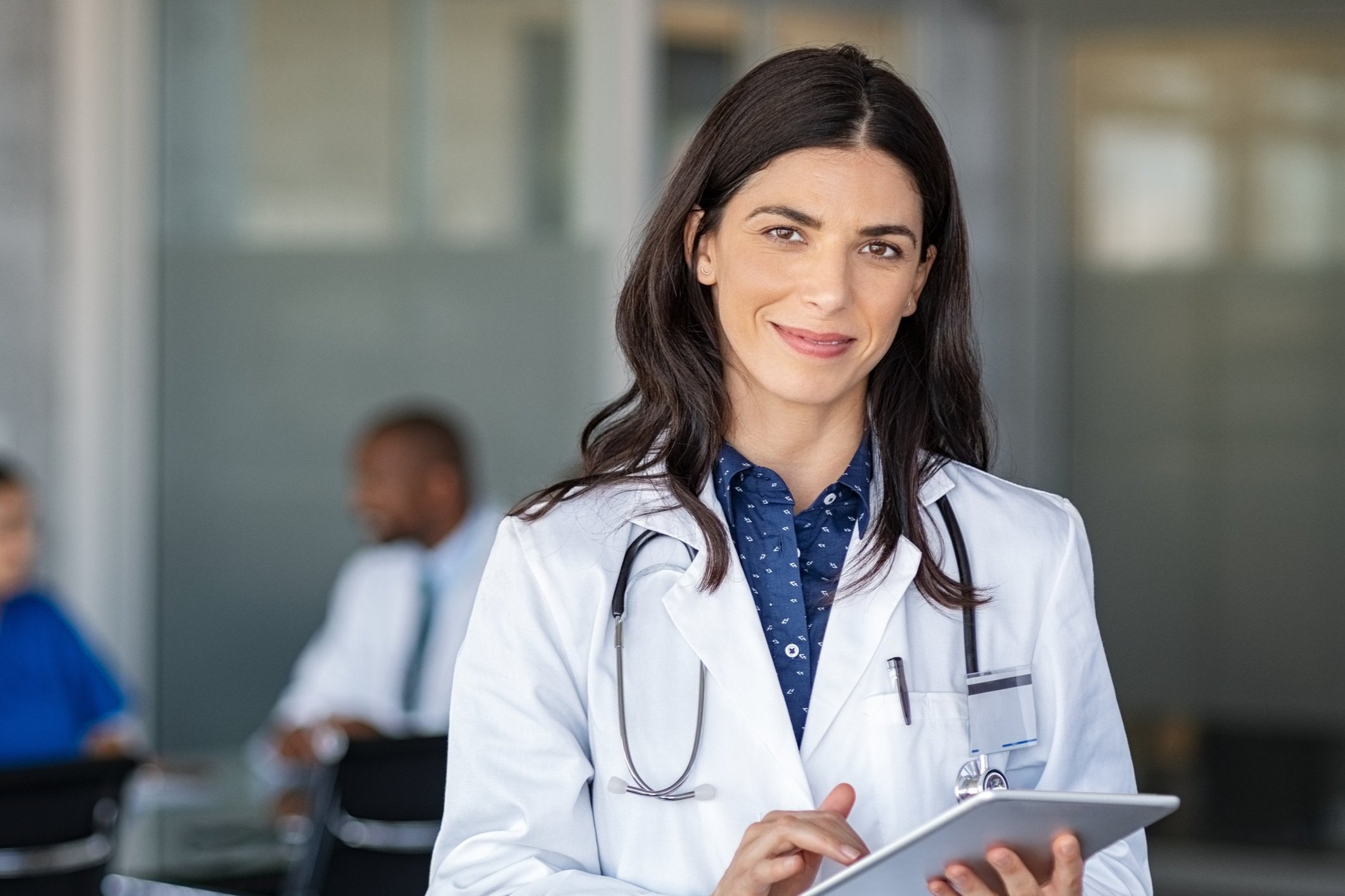 Group of diverse healthcare professionals standing outside, wearing scrubs and lab coats, smiling at the camera.