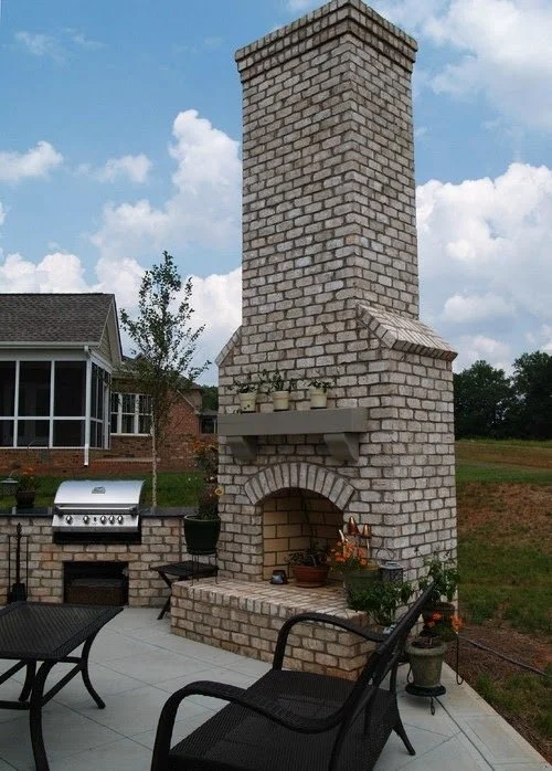 Outdoor brick fireplace with tall chimney, decorated with potted plants and outdoor furniture on patio.