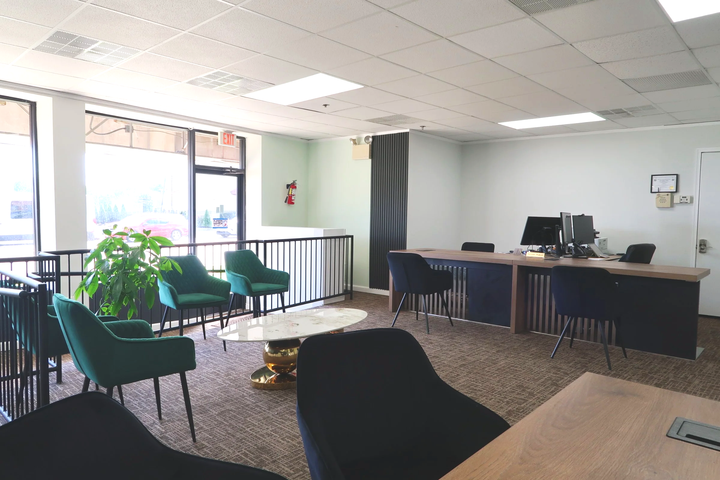 An office lobby with large glass windows, green and black seating, a marble coffee table, and a reception desk with computers.