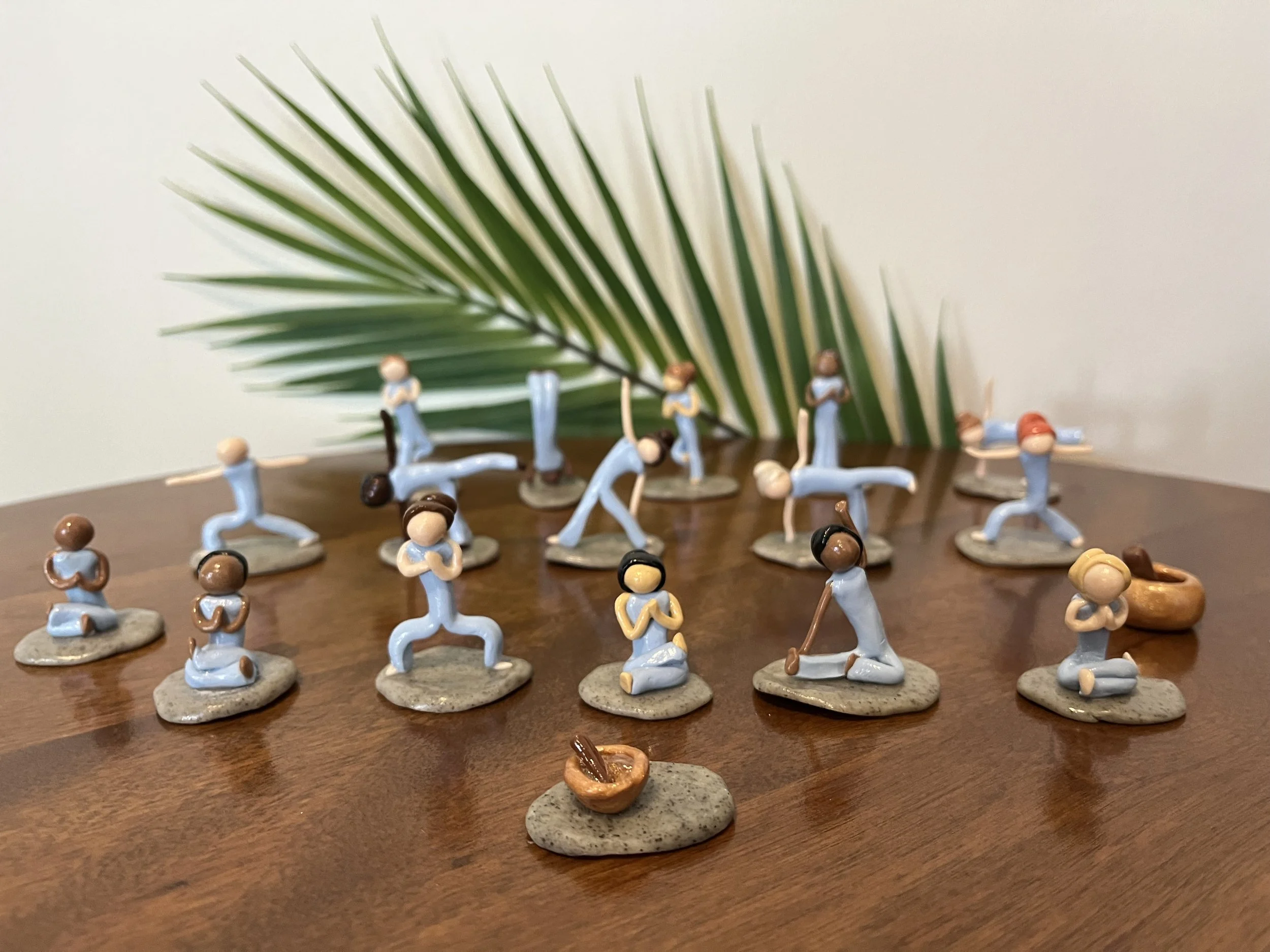 Sixteen clay yogi sculptures by Alexis Velez Pearlman practicing in various poses.