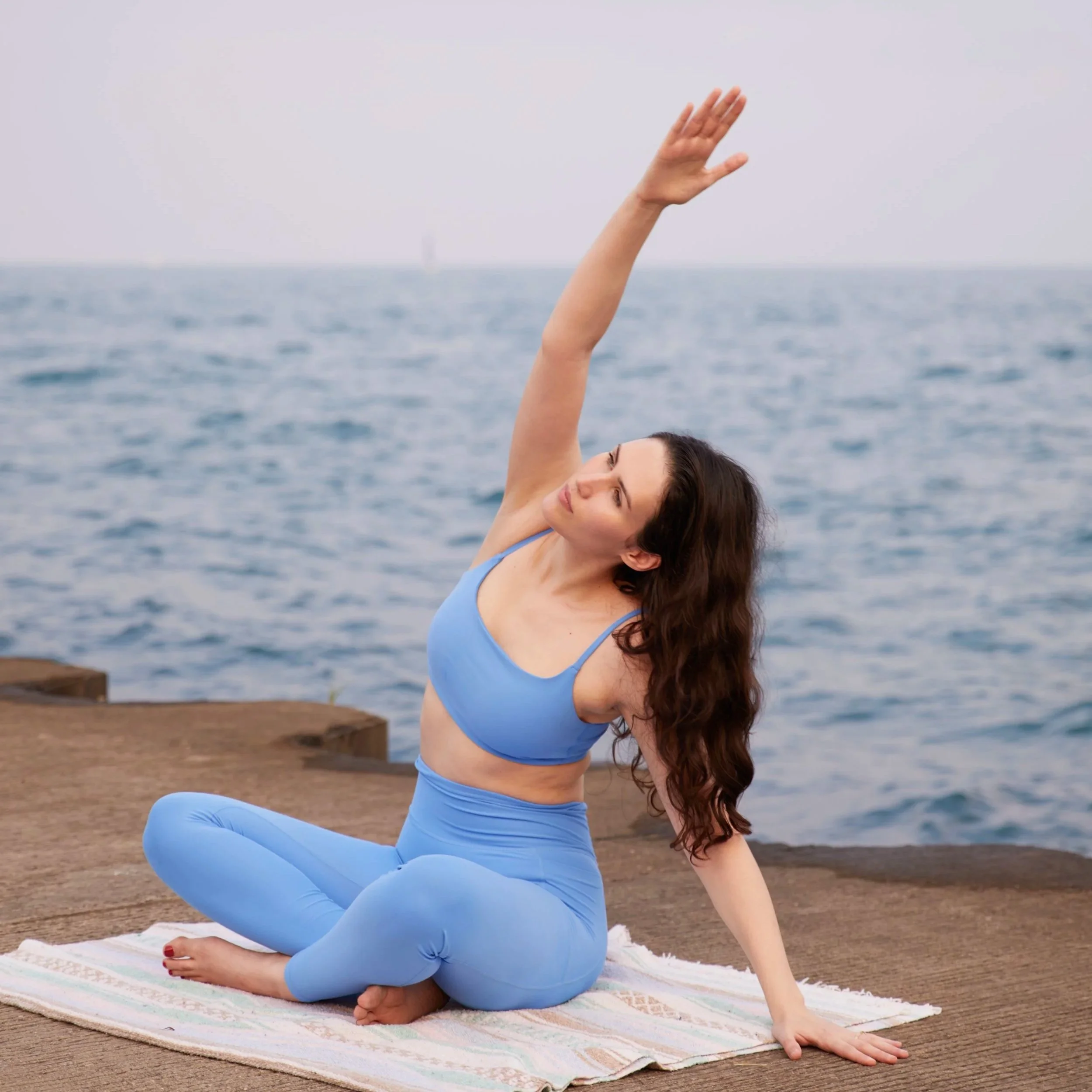 Alexis Velez Pearlman practicing a seated side stretch on a pier by the lake.