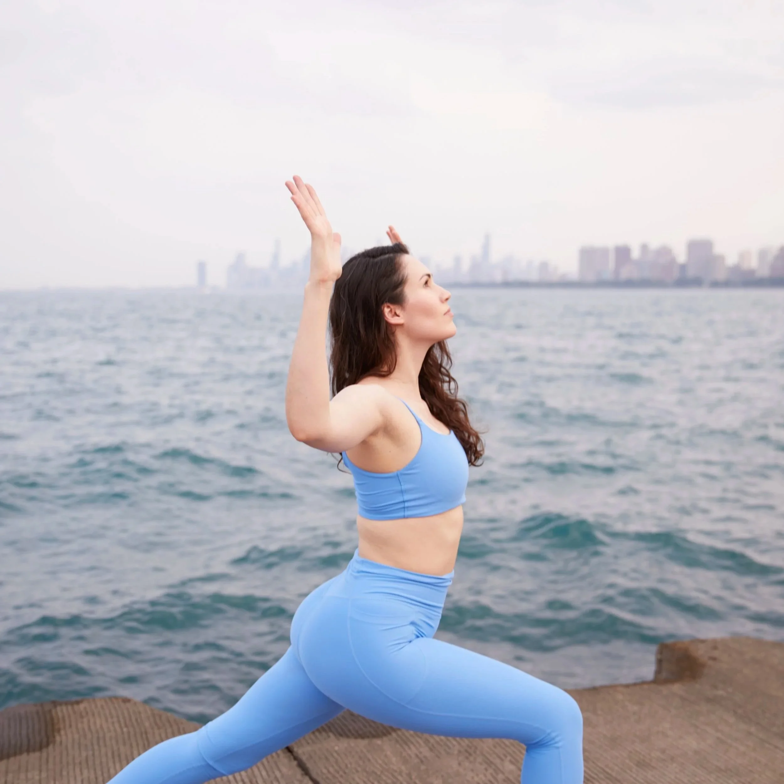 Alexis Velez Pearlman practicing a crescent lunge pose with cactus arms on a pier by the lake.