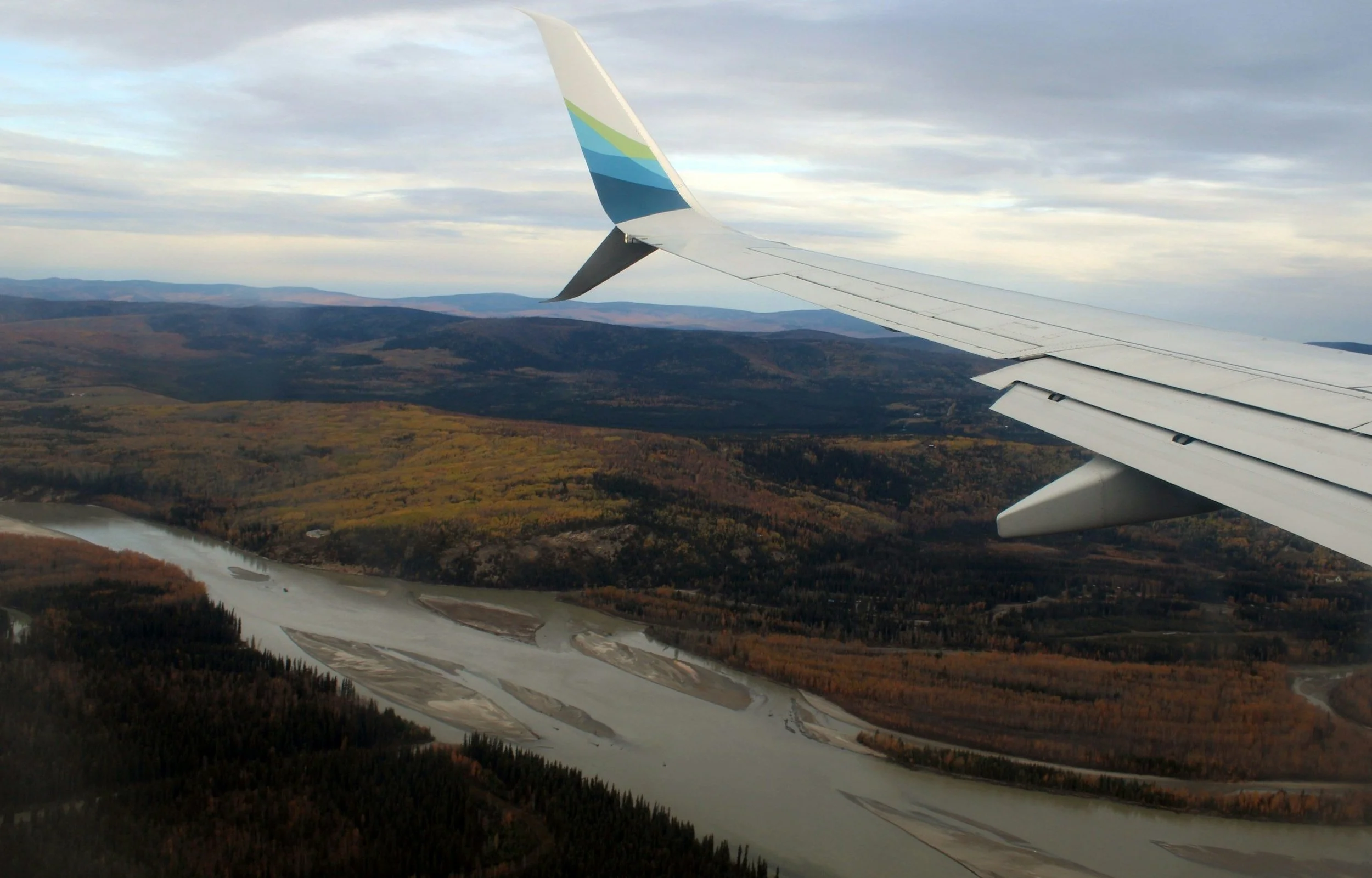 View from airplane window over landscape with river and forested hills