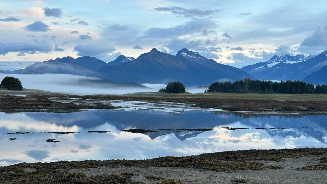 Mountain landscape with a calm body of water reflecting the mountains, trees, and sky.