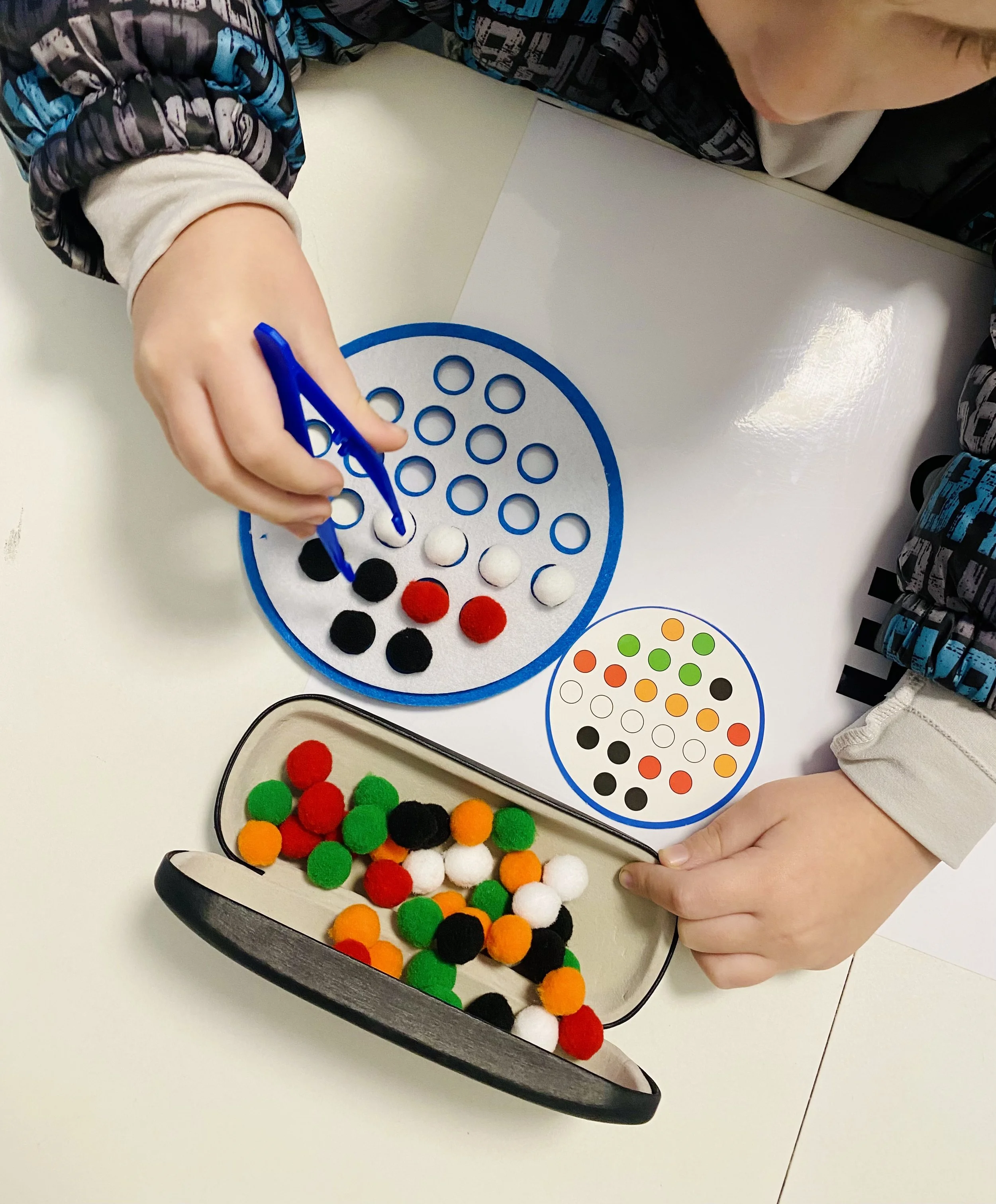 Un bambino gioca con palline di feltro di diversi colori e disegni, mentre sovrappone e ordina le palline su un tabellone con fori e grafica colorata.