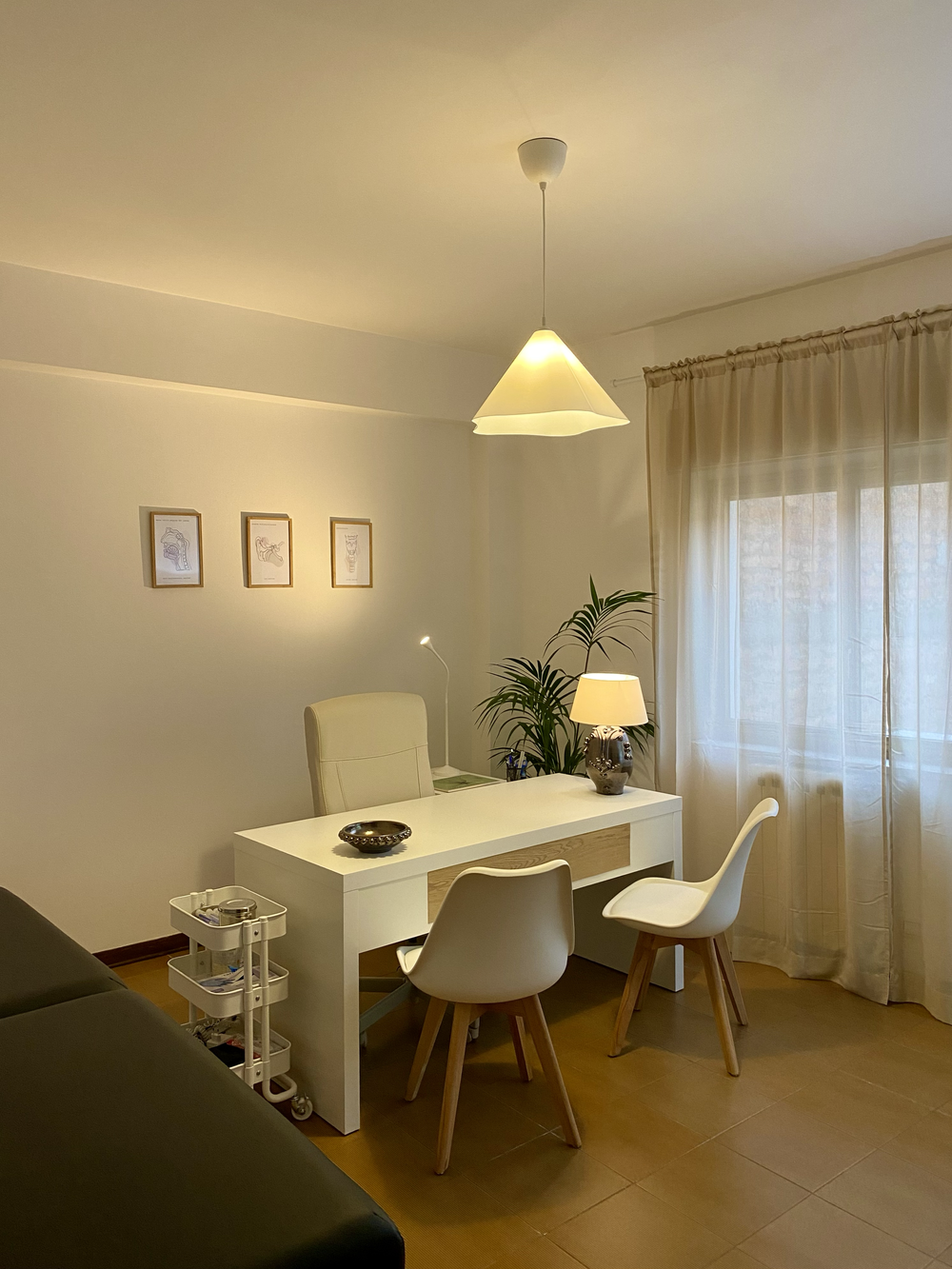 Sala di terapia con scrivania bianca, sedie e pianta vicino alla finestra