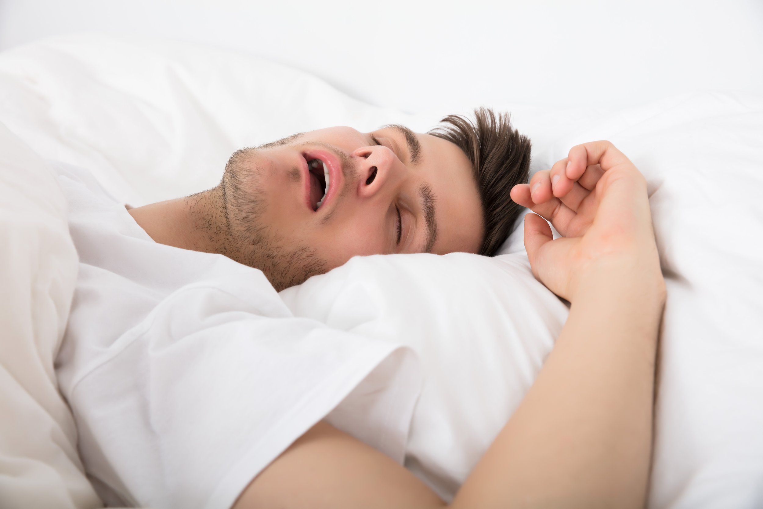 Young man lying on a bed with white sheets, appearing to be asleep or resting.