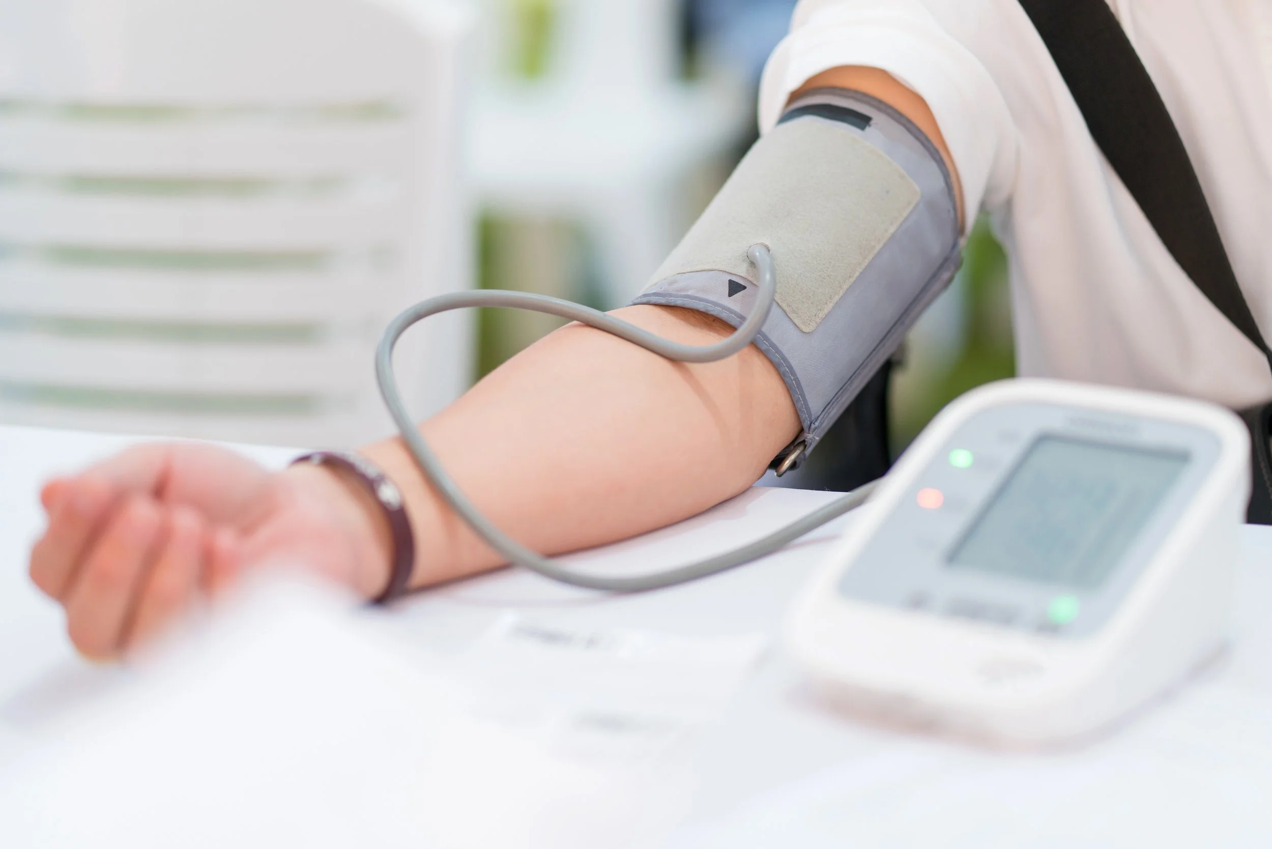 A person having their blood pressure measured with a cuff on their upper arm, connected to a digital blood pressure monitor on a white table.