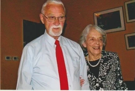 Quinn and Verna Smet standing together indoors, with framed artwork behind them.
