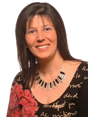 Une femme souriante avec des cheveux bruns, portant un collier noir et un haut à motifs rouge et noir avec du texte en français.