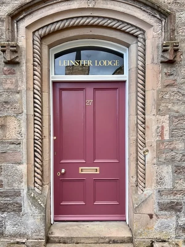 A closed purple front door with the number 27, set in a stone building with an arched window above that reads 'LEINSTER LODGE'.