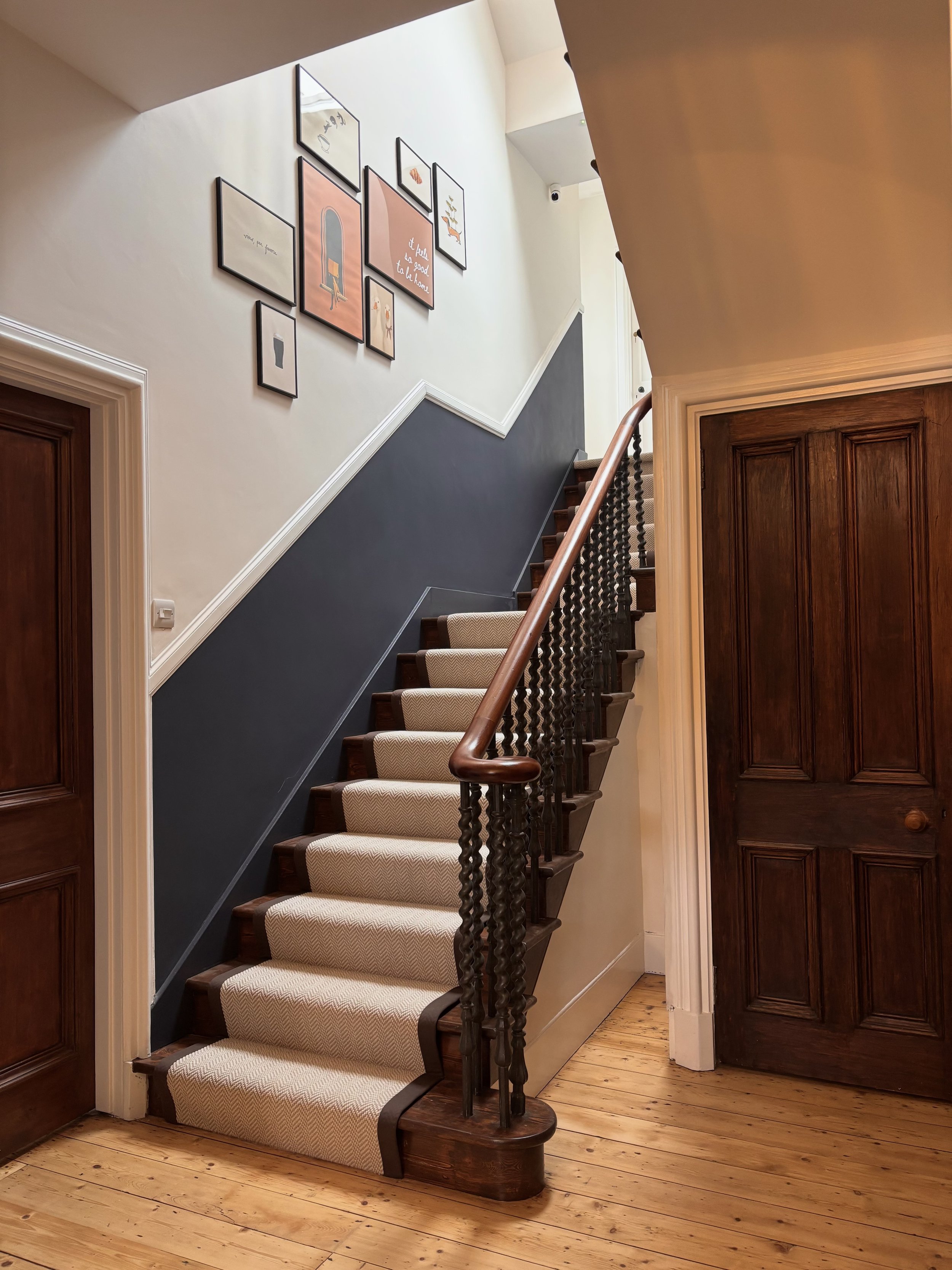 Interior view of a staircase with a dark blue wall, wooden handrail, and framed artwork on the wall, including signs with positive messages.