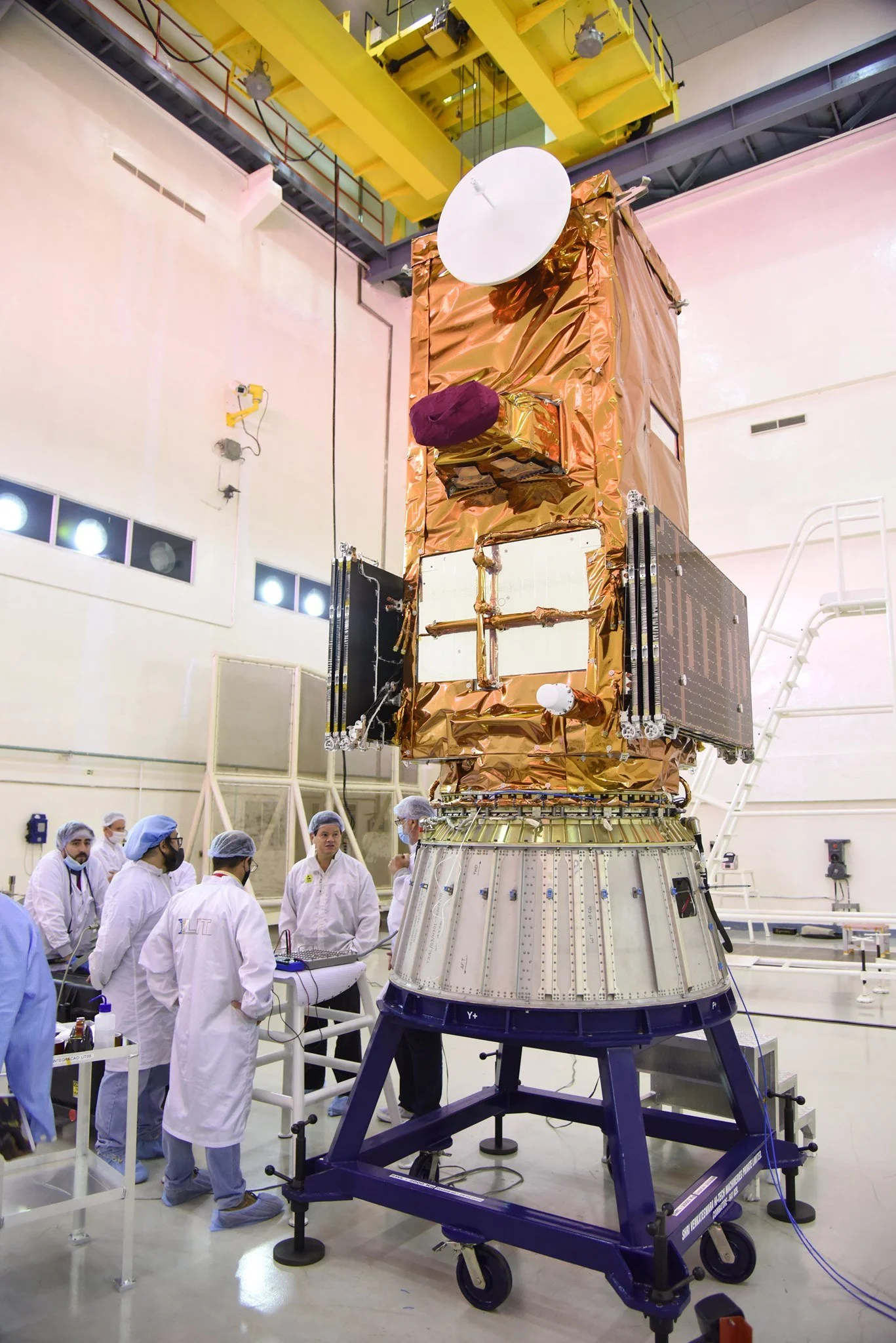 An engineering team in cleanroom suits around a satellite in a high-tech laboratory.