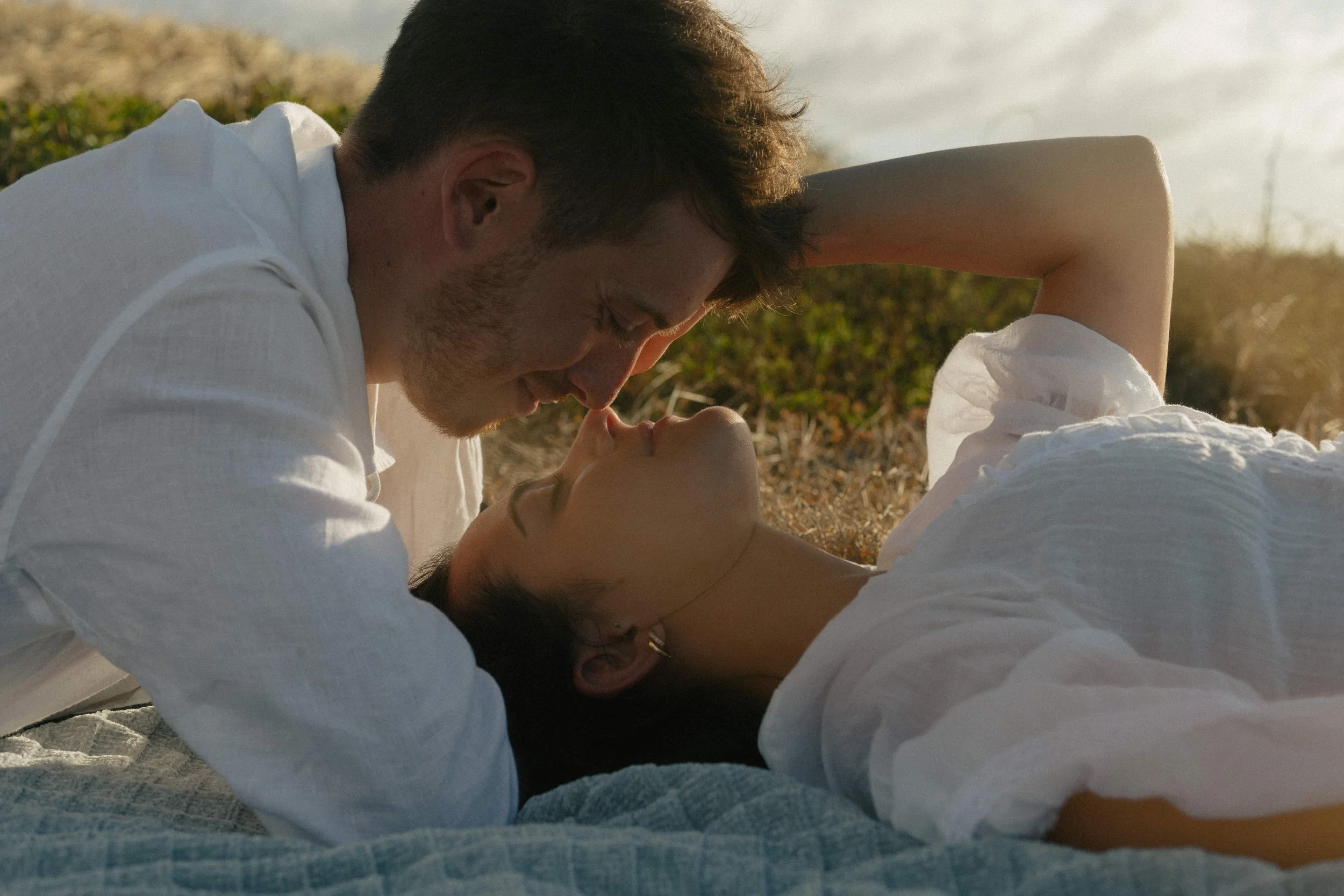 Husband and wife laying along the coast of big island, Hawaii at sunset, romantic moment