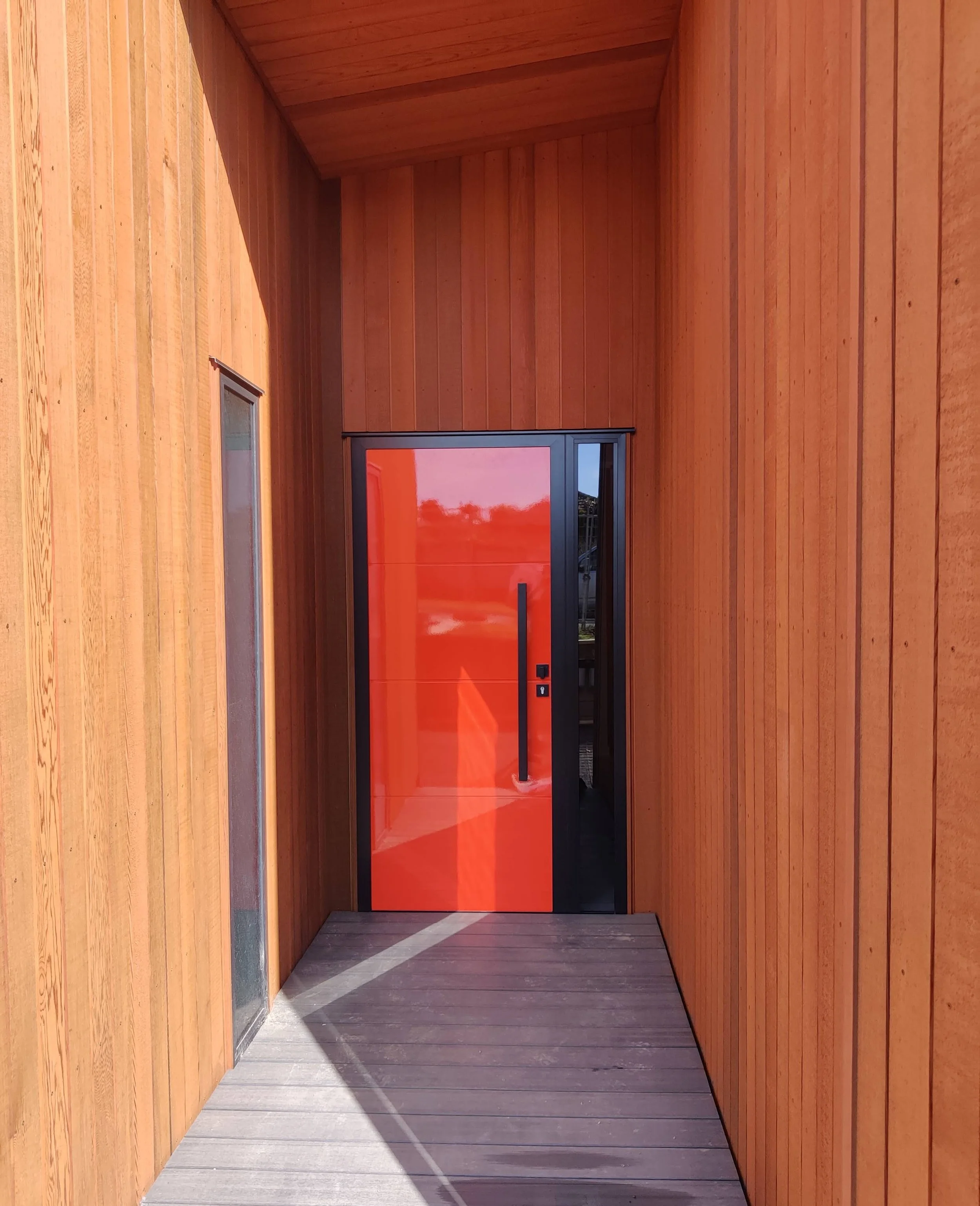 A modern wooden entryway with a vibrant orange front door and a sleek black handle.