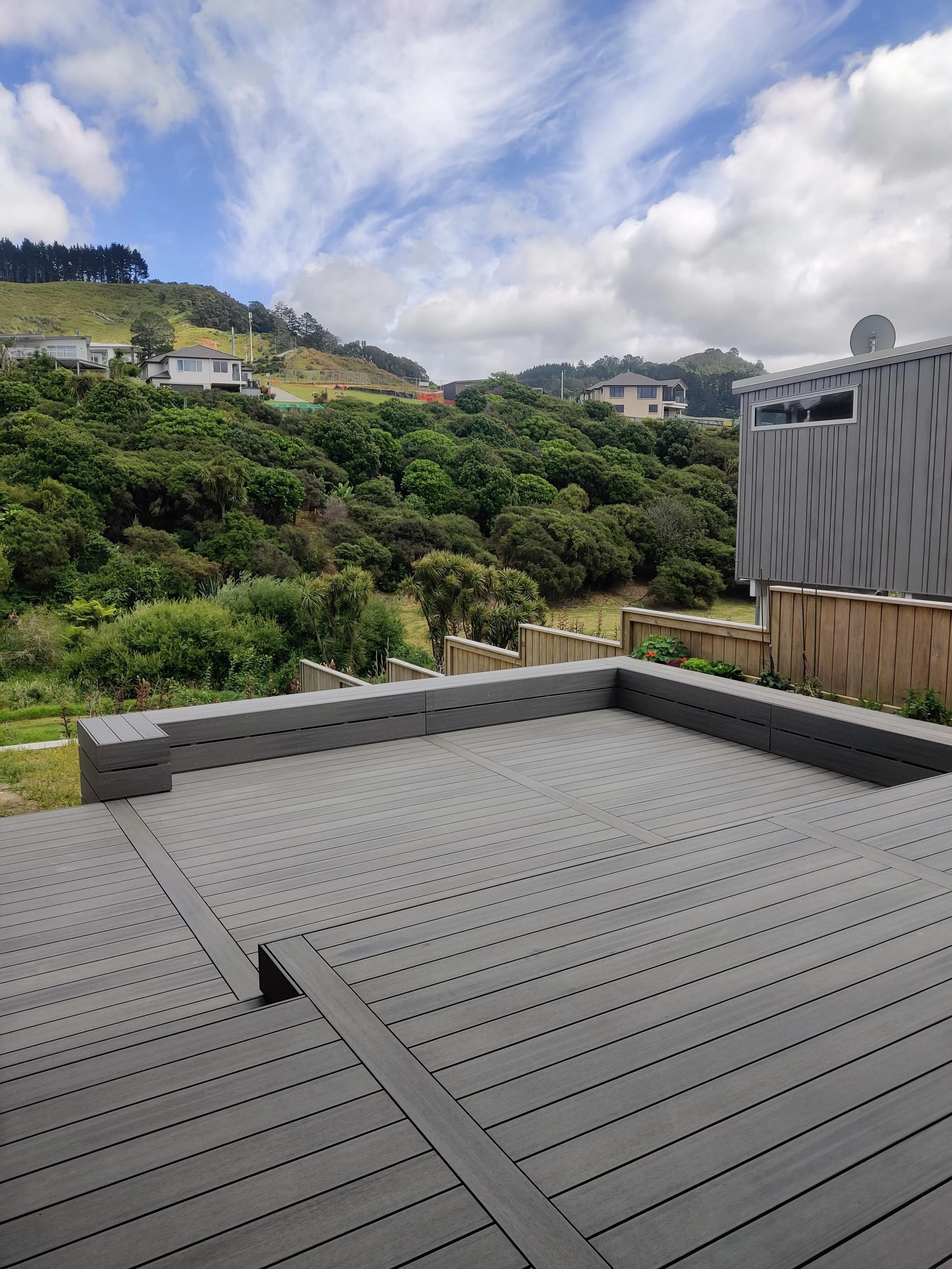 Sunset view from a wooden deck with benches and steps beside a house, surrounded by trees and grass.
