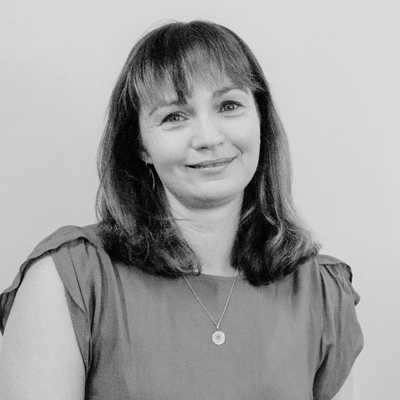 A photo of Victoria Griffiths, a woman with shoulder-length hair smiling at the camera, wearing a short-sleeved top and a necklace.