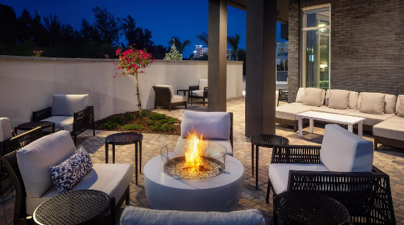 Outdoor patio with seating area featuring cushioned chairs, a fire pit, and an outdoor sofa, on a evening with a darkening sky.
