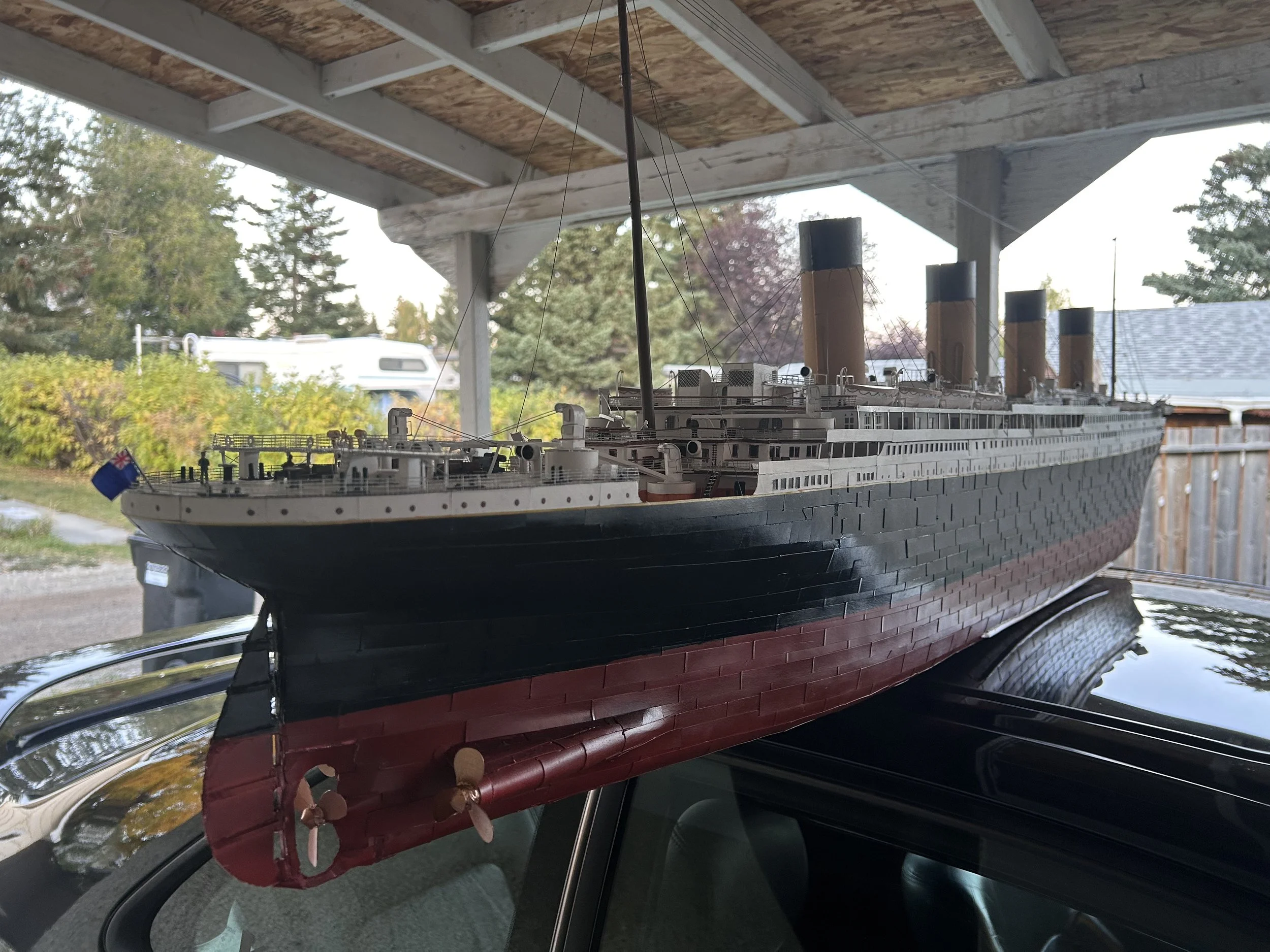 A detailed model of the Titanic ship, with black hull, red bottom, and four large smoke stacks, displayed outdoors on a black surface.