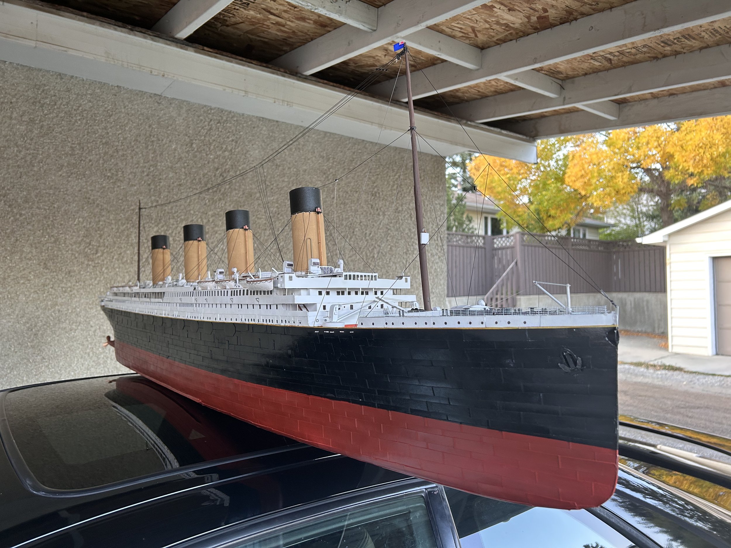 A detailed model of the Titanic ship placed on a car roof, with house and trees in the background.