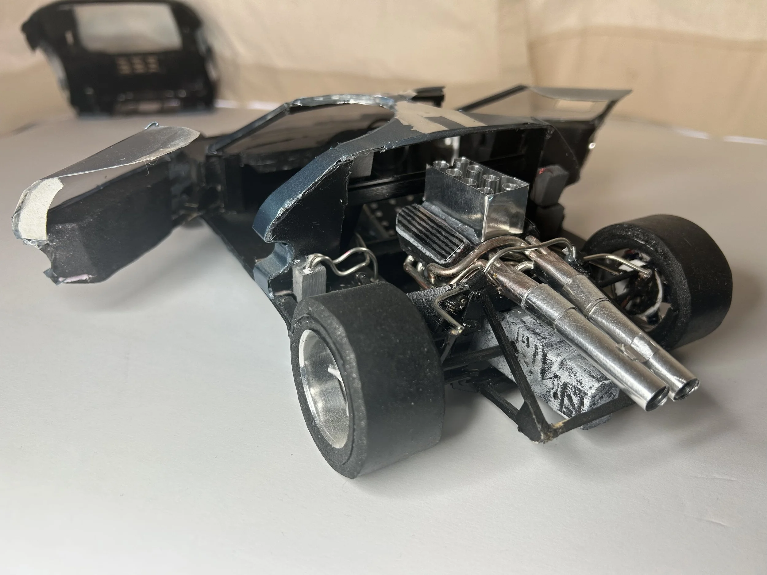 Model race car with exposed engine, black body, and black tires on a white surface.