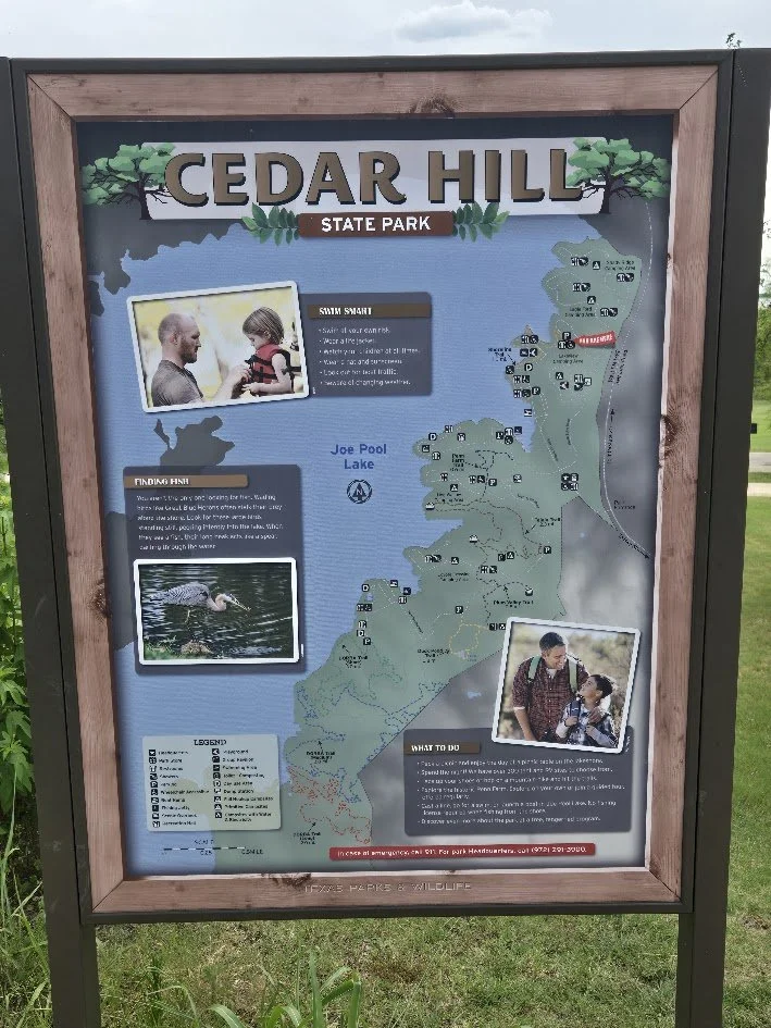 Cedar Hill State Park informational sign featuring a map of the park, notes on swimming safety, a bird picture, and photos of visitors enjoying the park during a field trip with Beulah's Bunch Camp organizers.