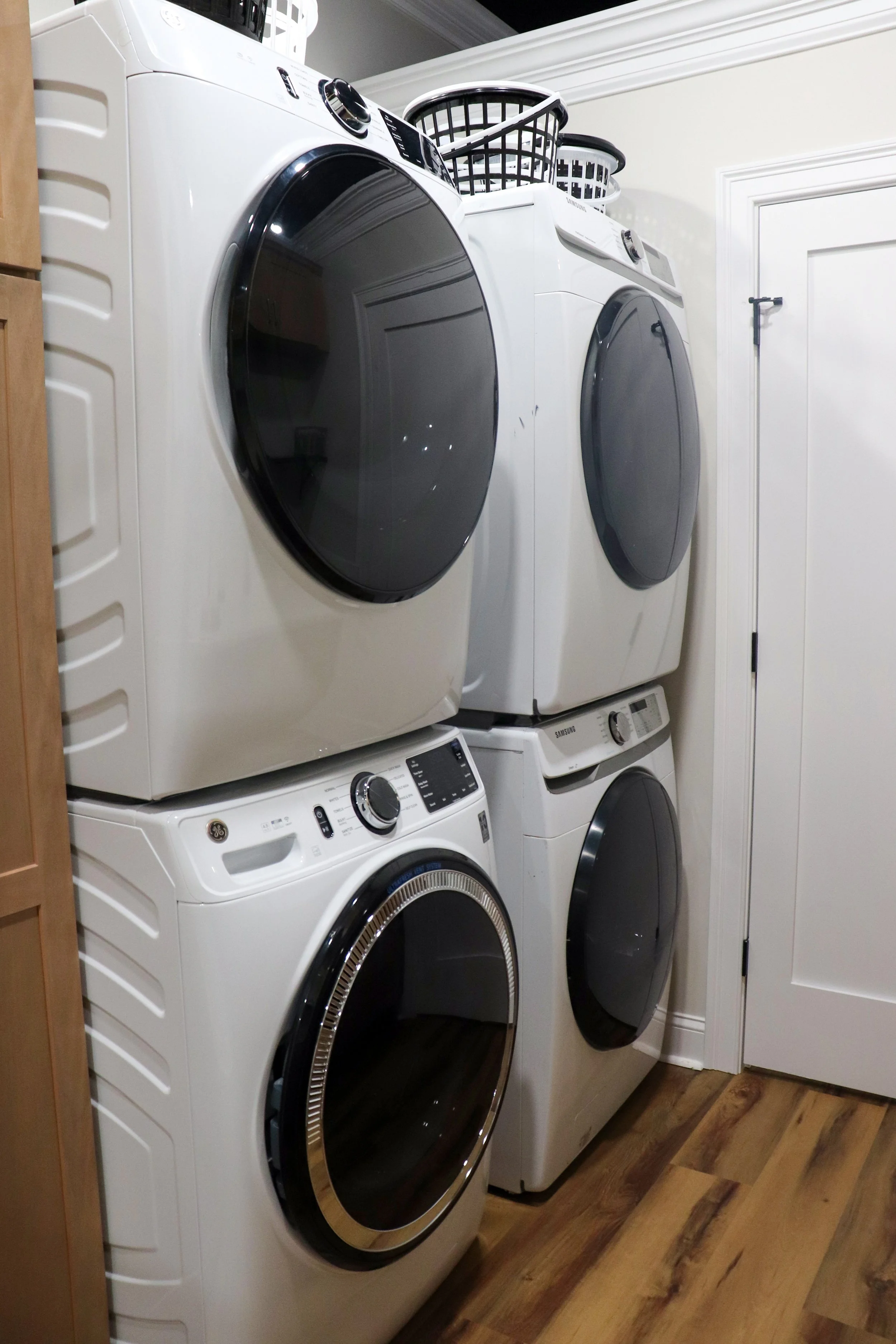 Four front-loading washing machines stacked vertically in a laundry room with a laundry basket on top of the upper machines.