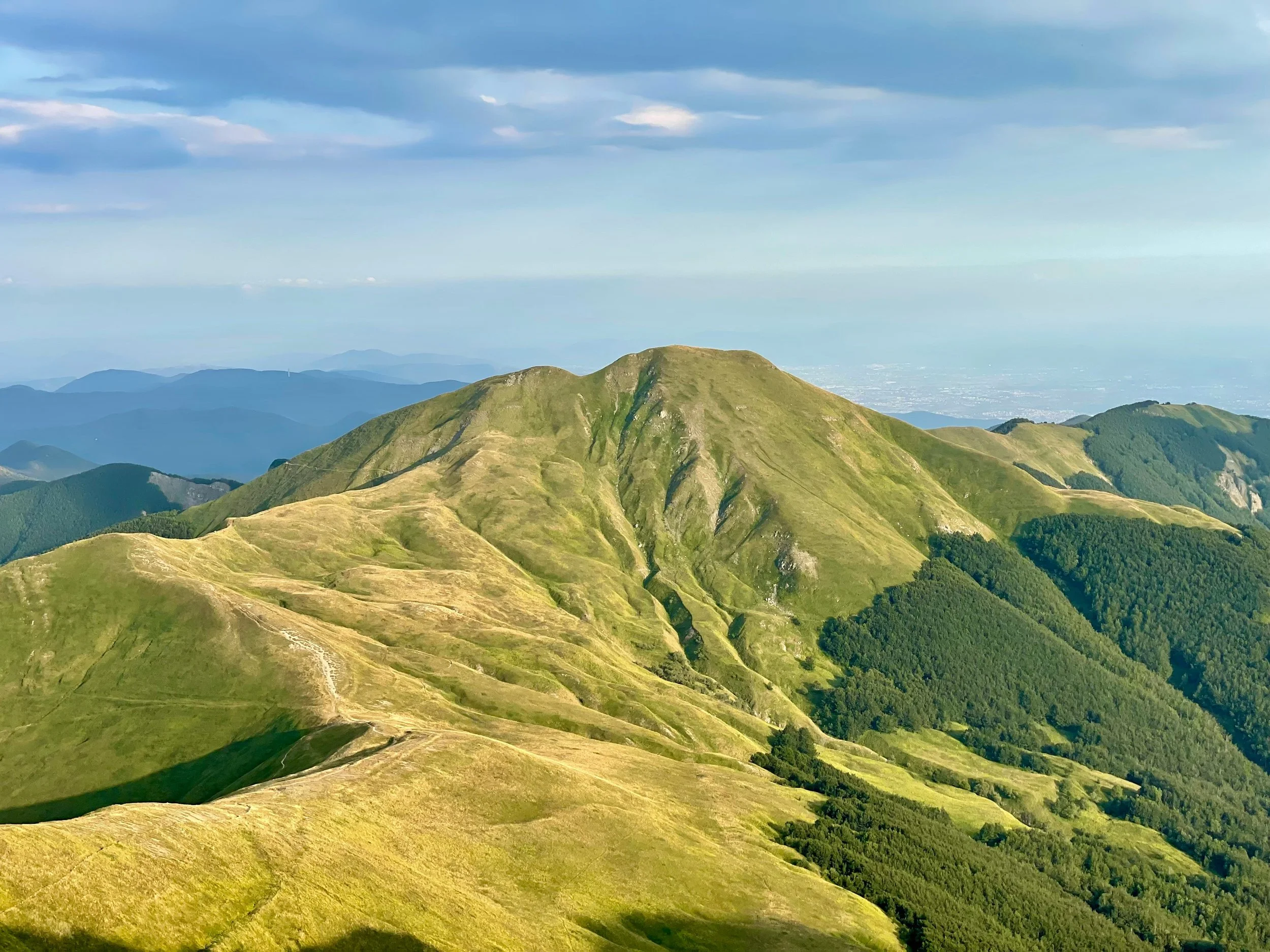 A mountain range with green grassy slopes and rolling hills under a partly cloudy sky.