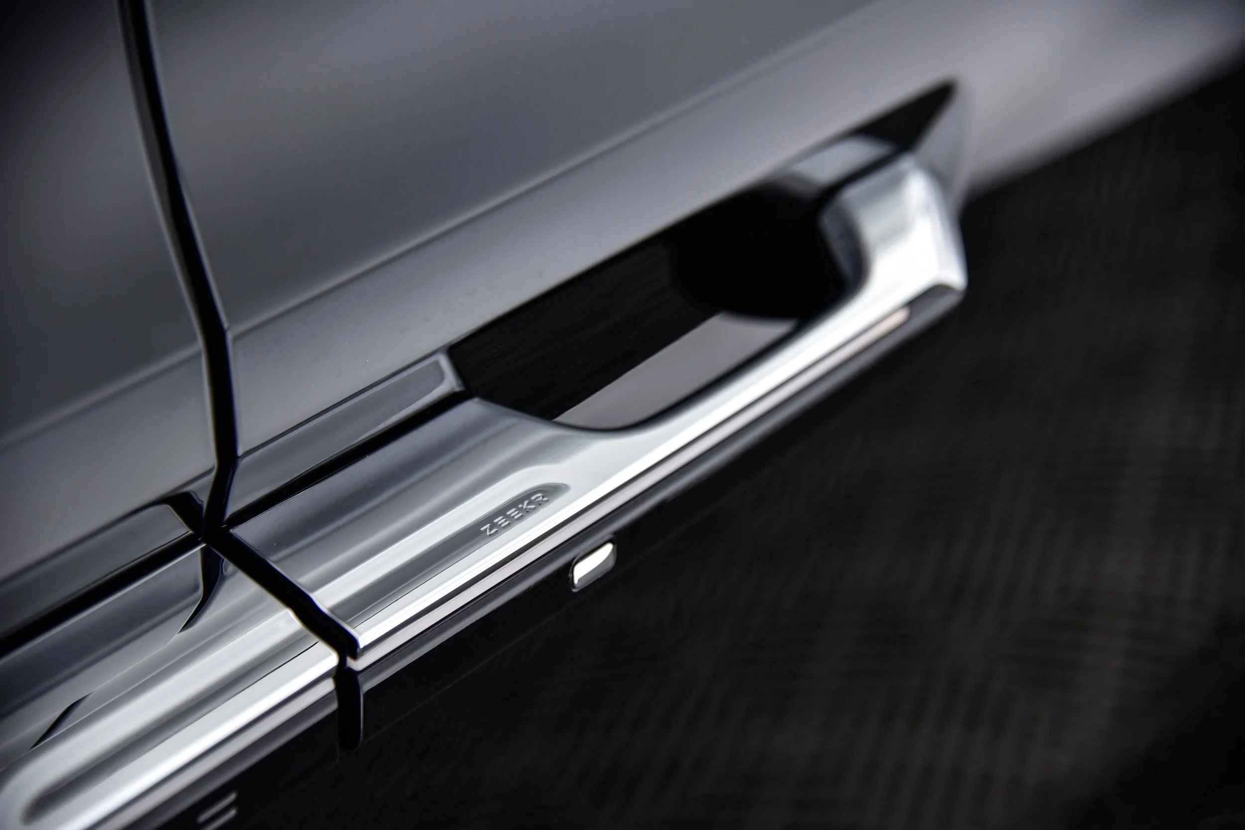 Close-up of a black and silver door handle on a dark-colored car.