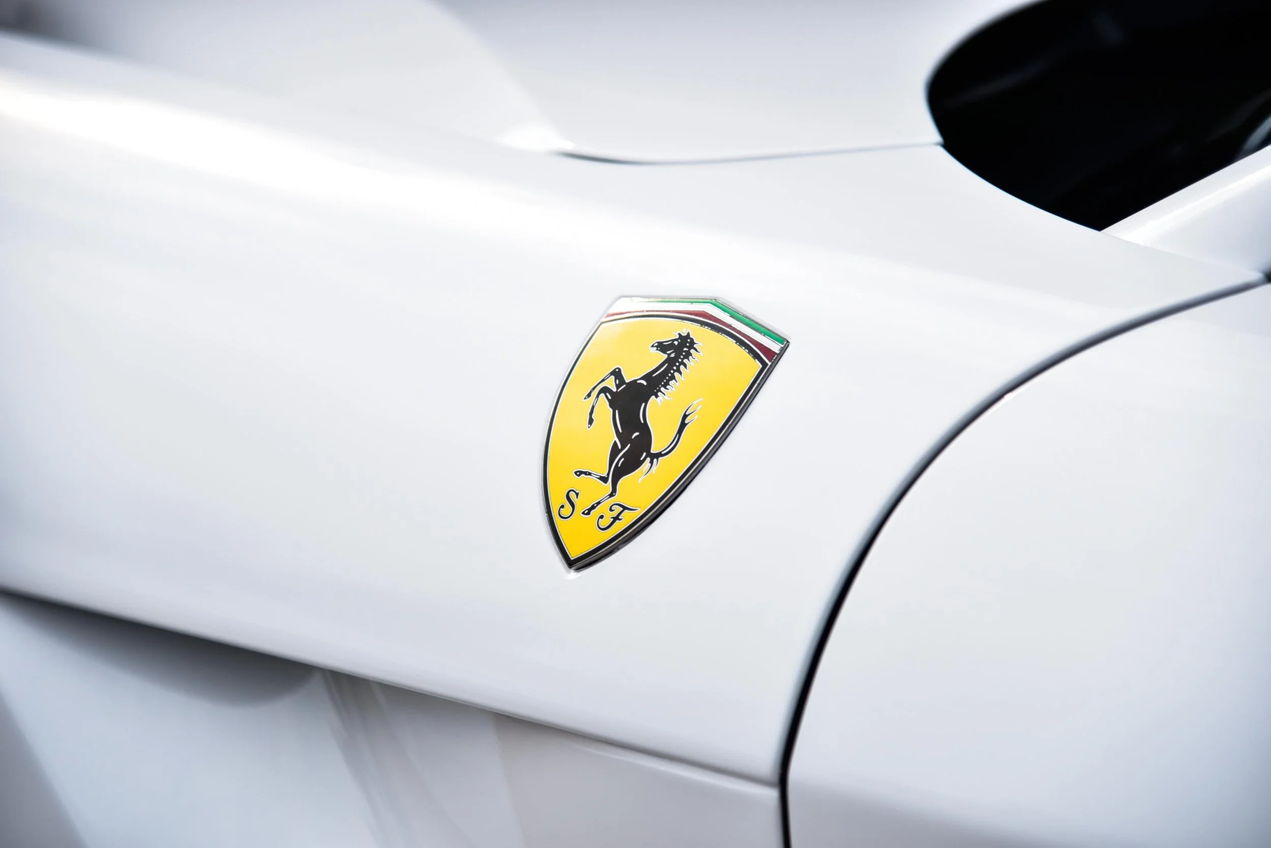 Close-up of a white Ferrari with a yellow shield emblem featuring a black prancing horse and red, white, and green accents.