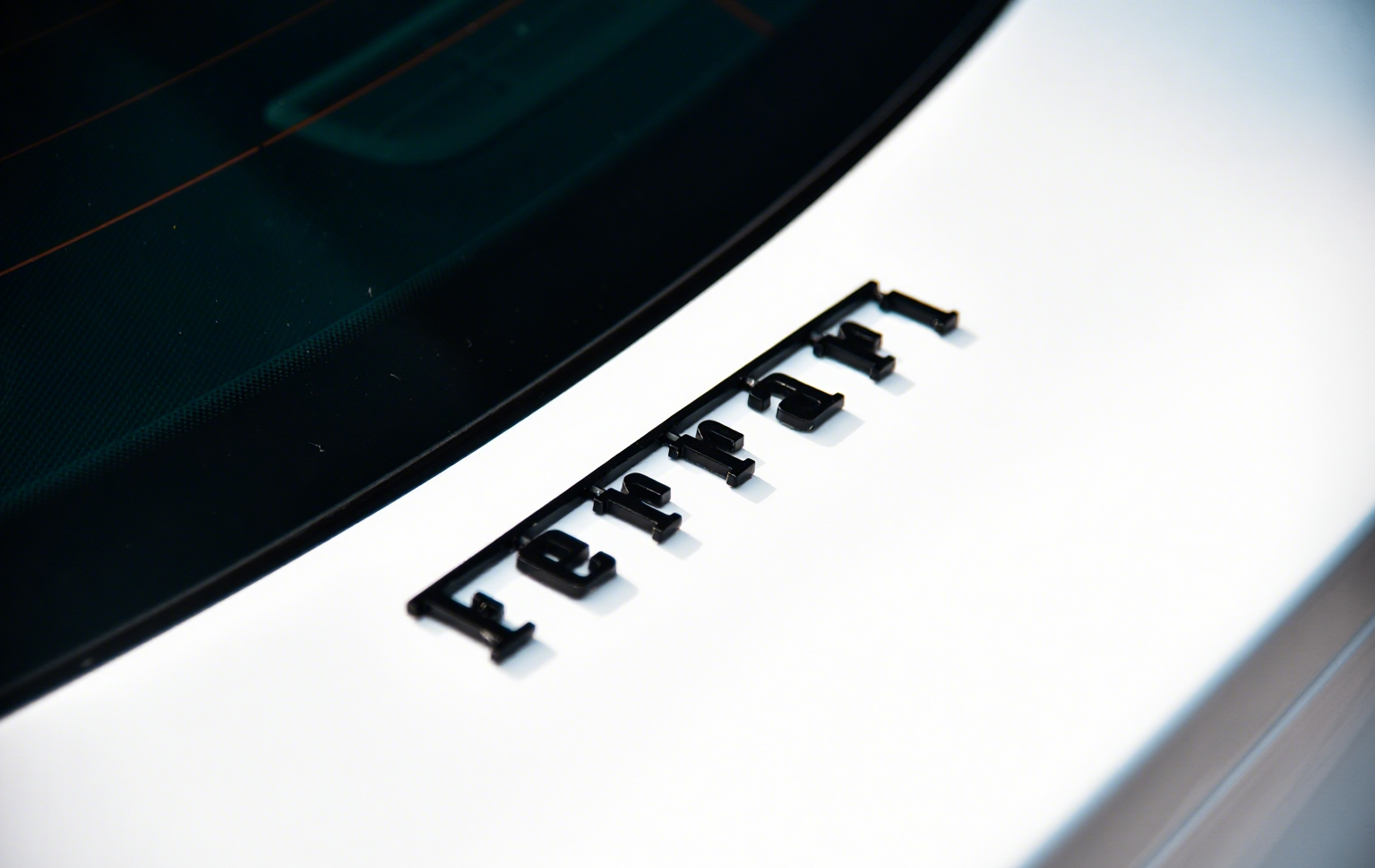 Photo of a Porsche logo on a car's white exterior with the car's rear window visible at the top.