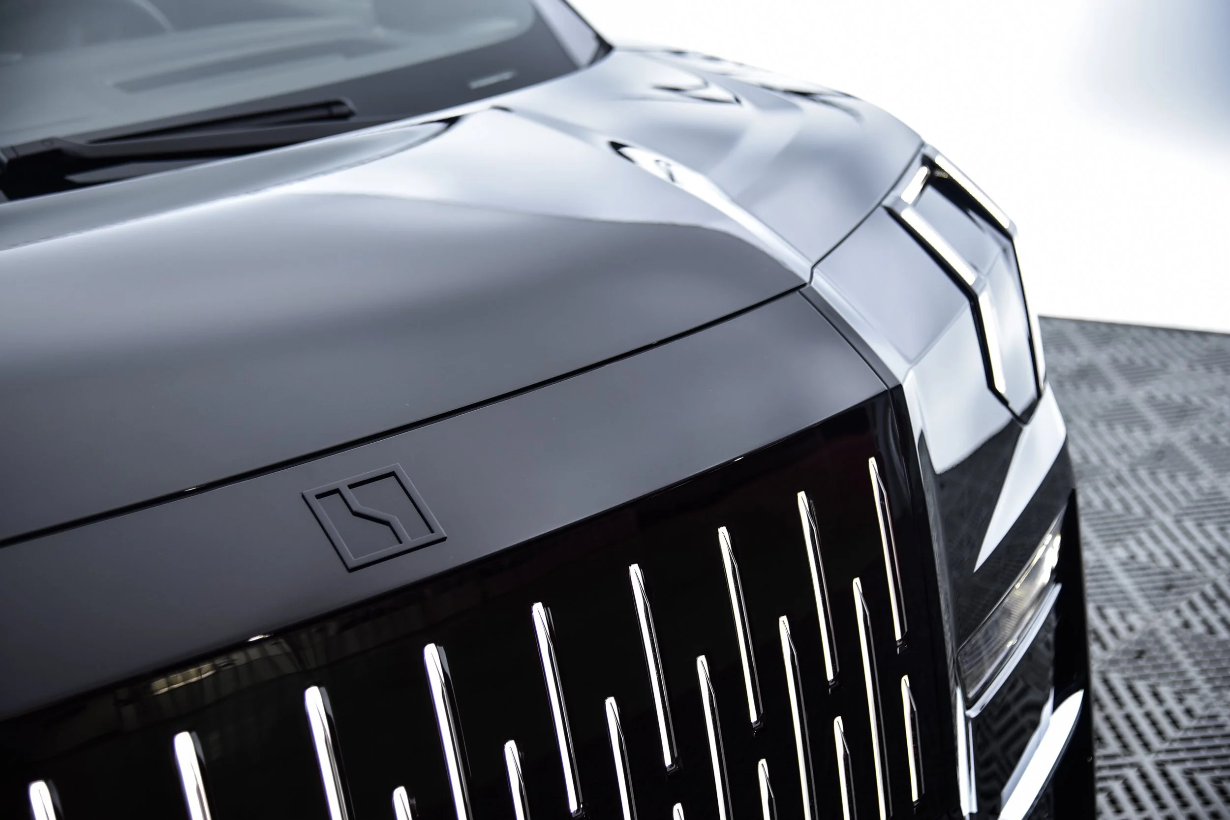 Close-up of the front of a sleek, black luxury car with vertical grille bars and modern angular design.