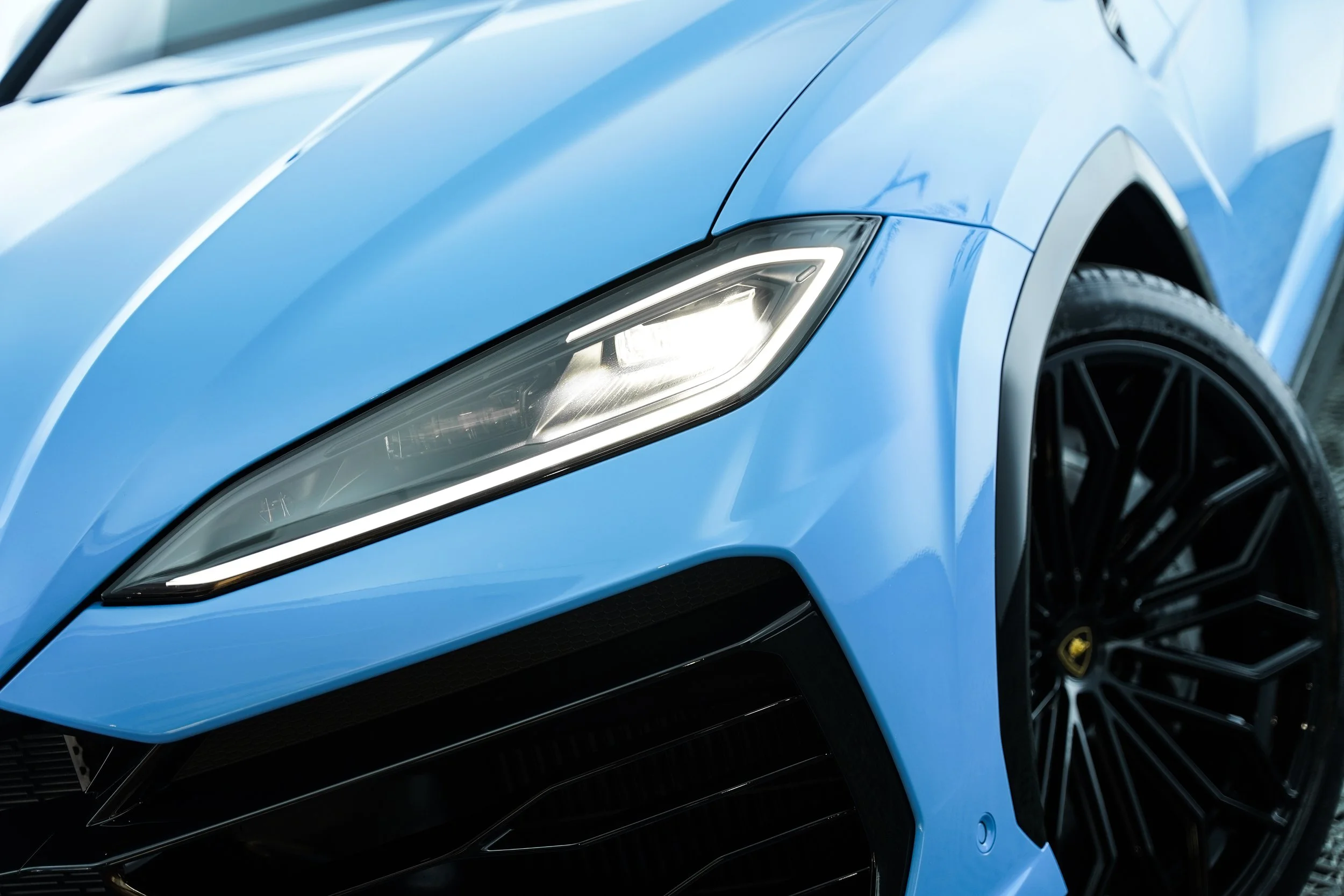 Close-up of the front of a blue sports car showing the headlight, front grille, and wheel.