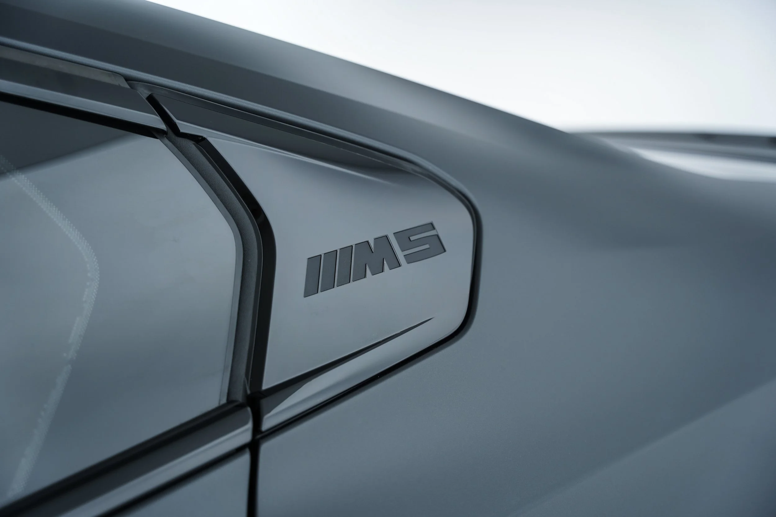 Close-up of a BMW M logo on a car door near the side window.