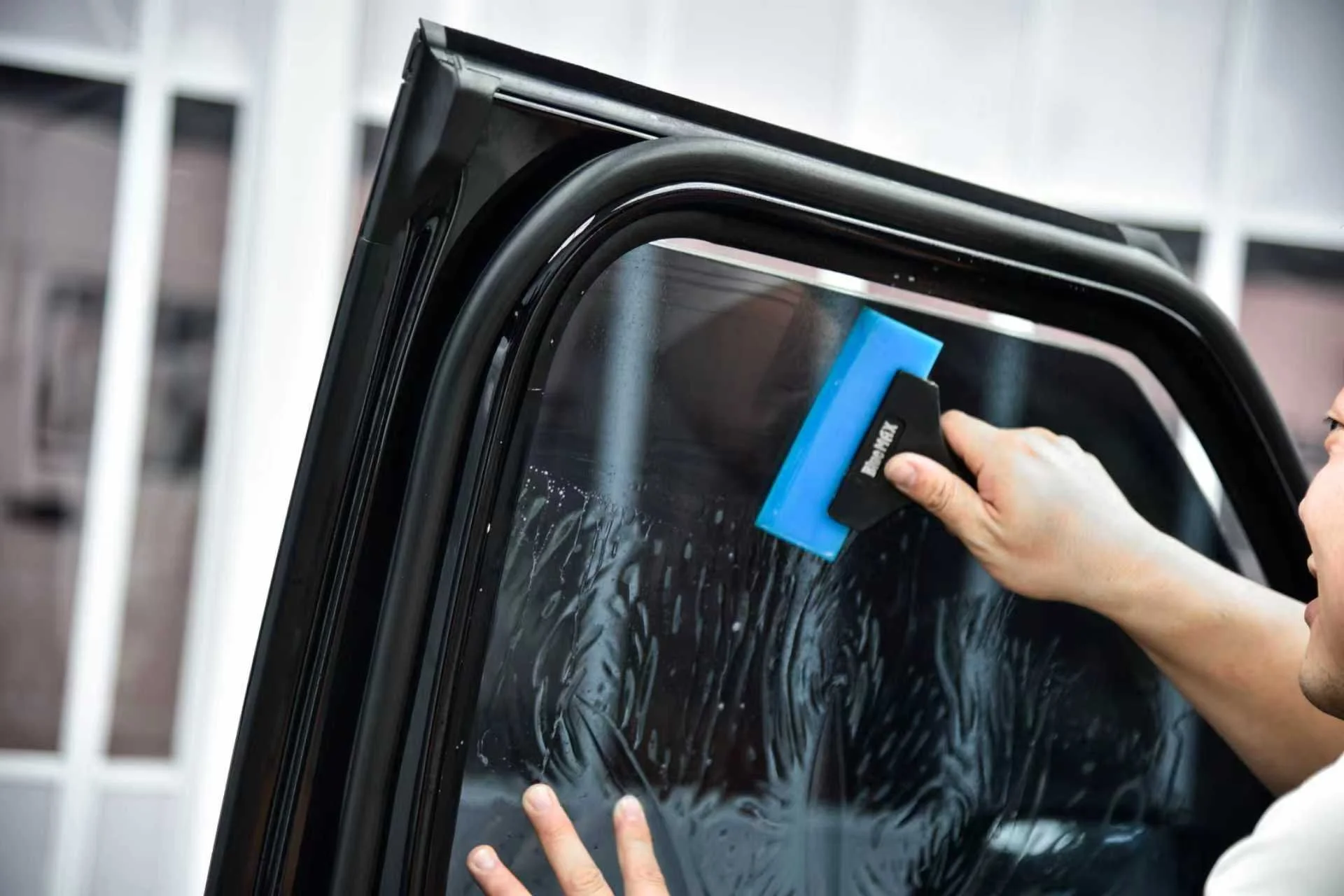 Person cleaning the window of a car with a squeegee.