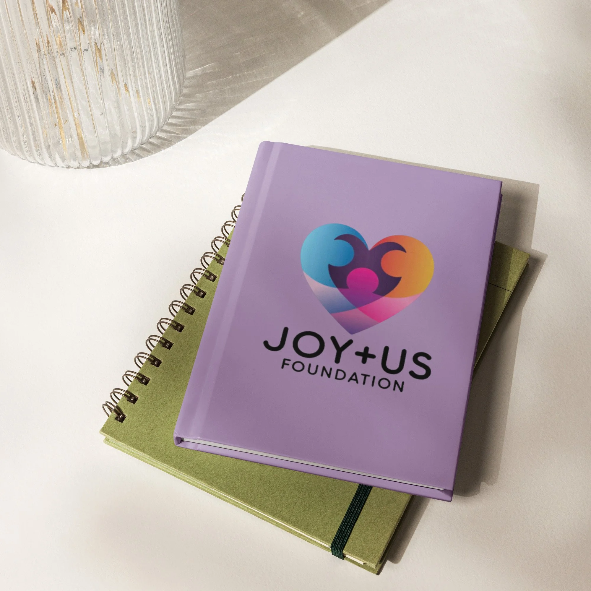 Purple book with logo of a smiling heart shape with two colors, blue and pink, and text 'Joy+Us Foundation' on the cover.