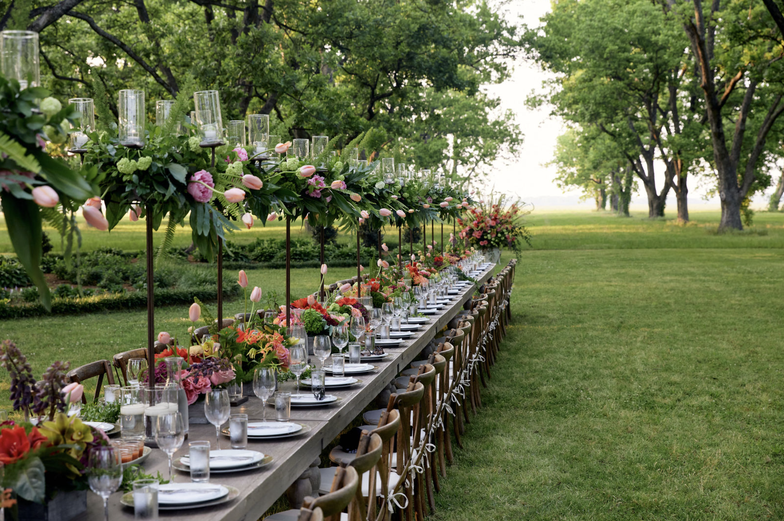 Long outdoor banquet table decorated with flowers and candles in a lush green garden
