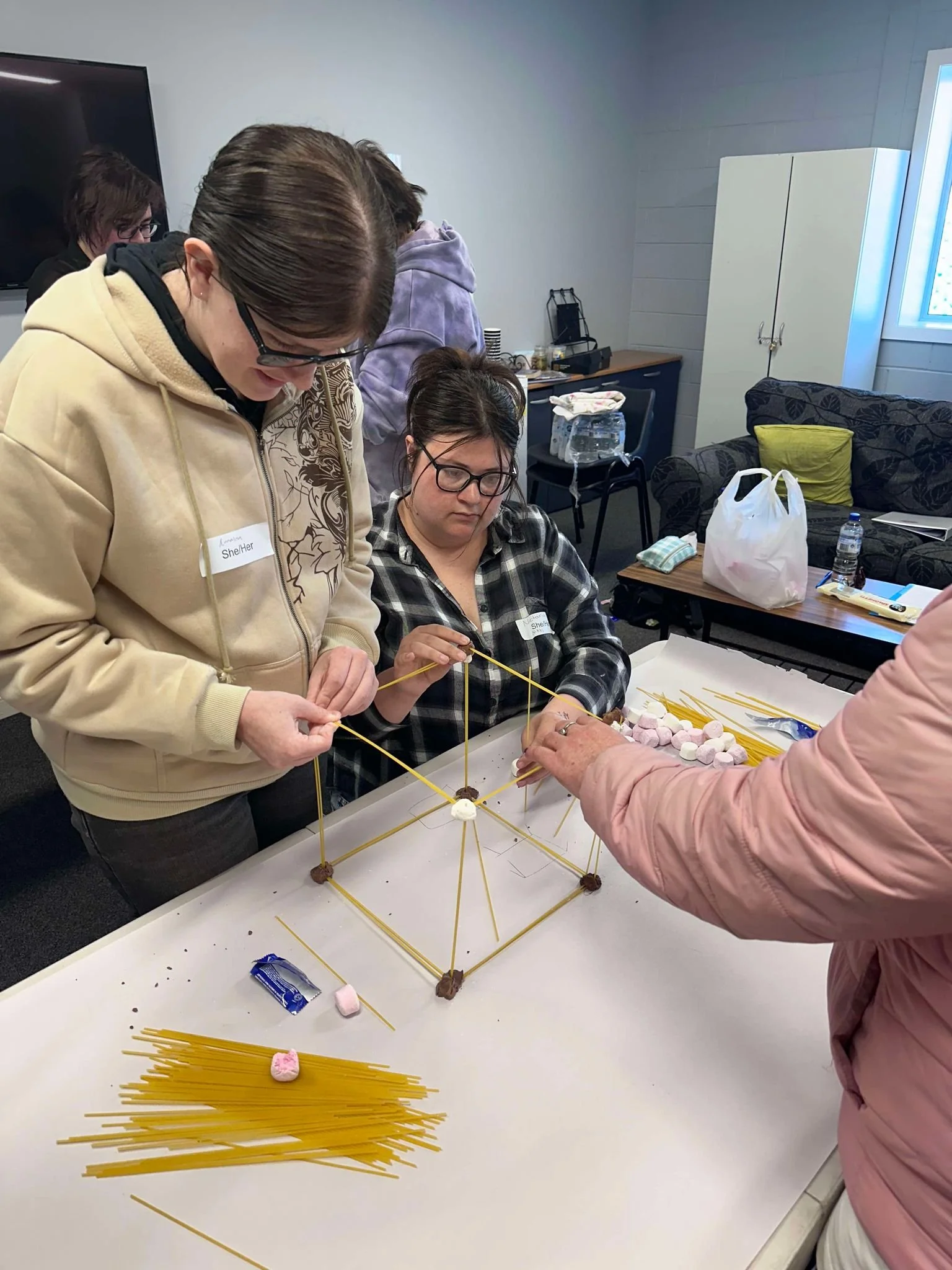 Three people working together to build a tower out of marshmallows and spaghetti.
