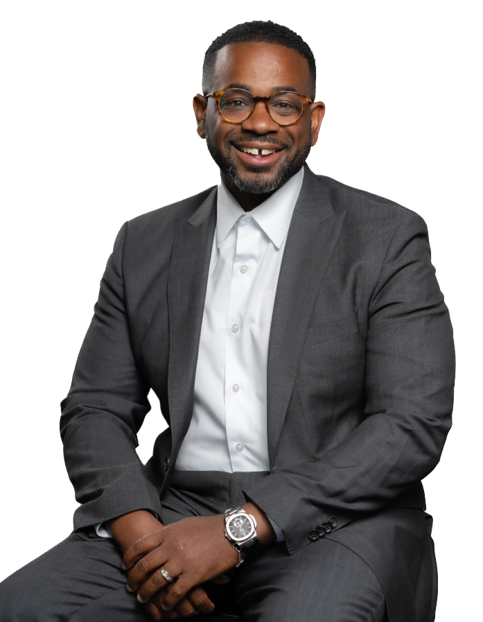 Devon Henry in a suit smiling, wearing glasses and a watch, sitting against a white background.