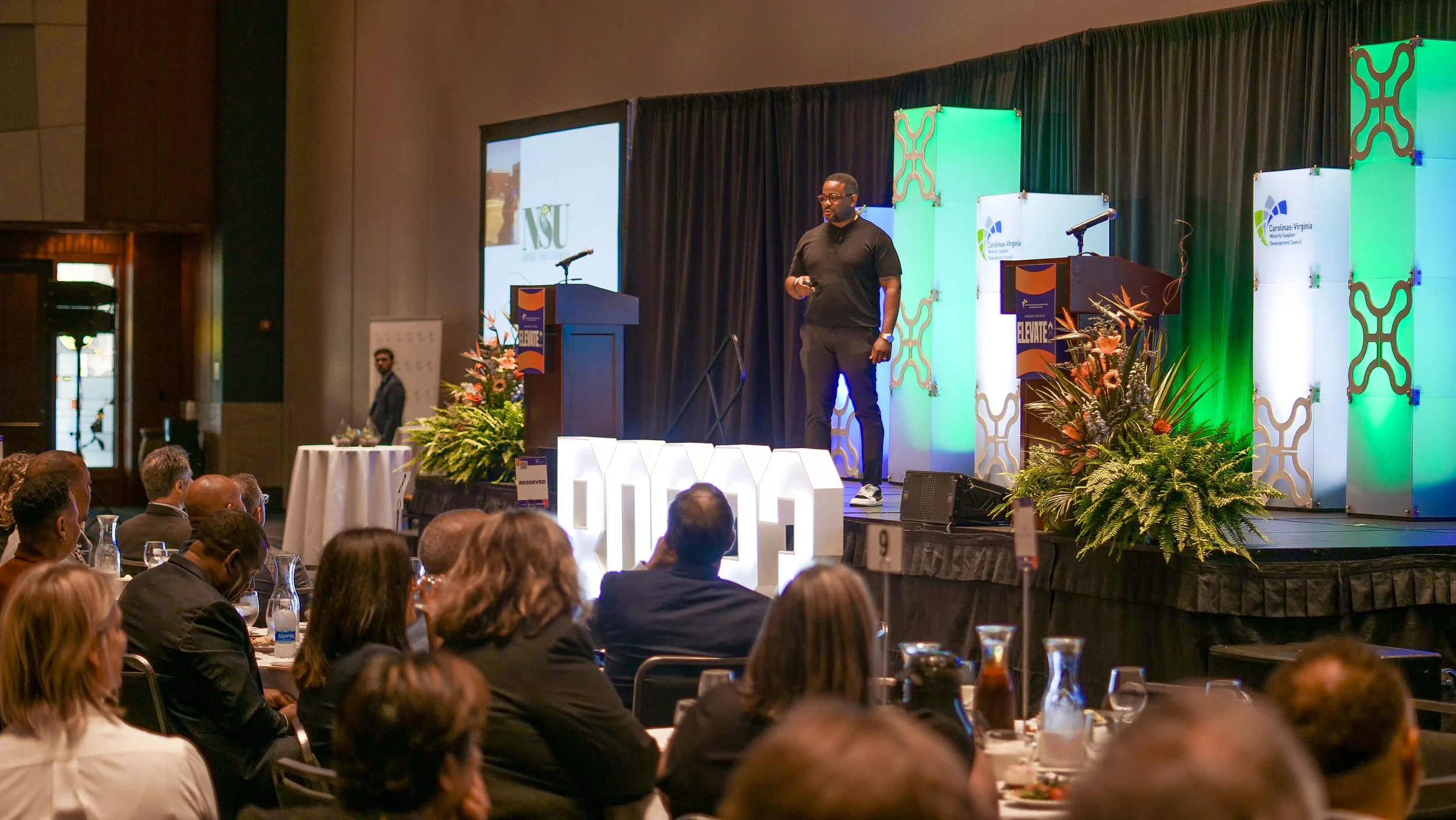 Devon Henry delivers a keynote onstage at a professional conference, with an engaged seated audience and vibrant stage lighting. Highlights executive speaking, thought leadership, and the power of live events to inspire, educate, and drive momentum.