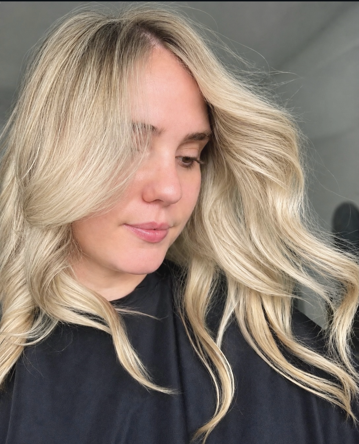 Close-up of a person with blonde hair, highlighted blonde, wearing a black top.
