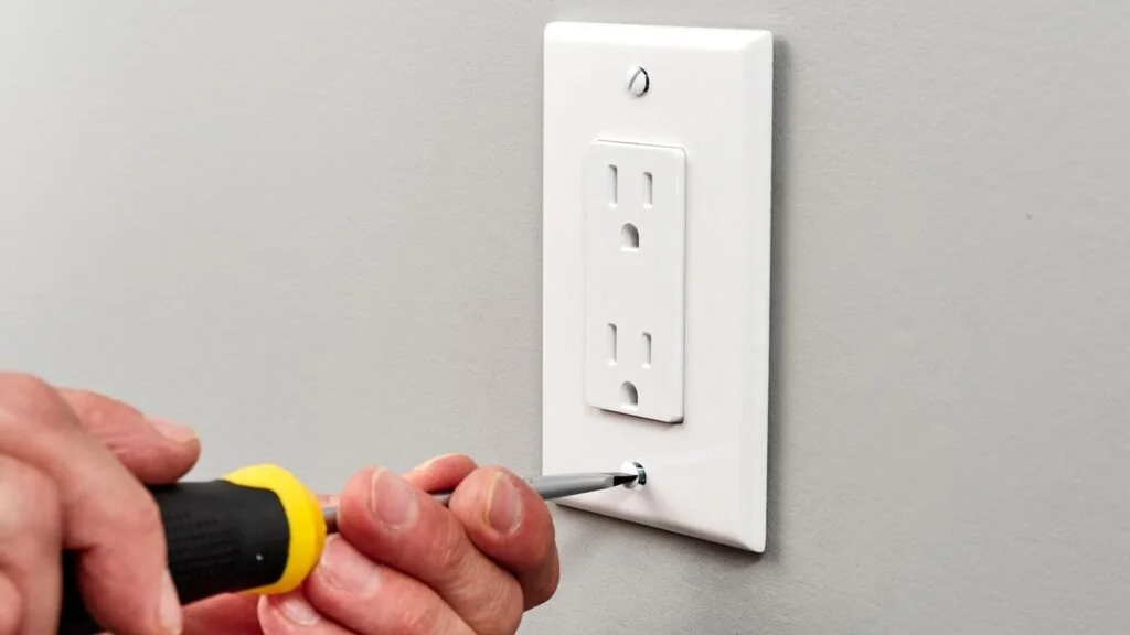 A person using a screwdriver to install or adjust a power outlet on a light gray wall.