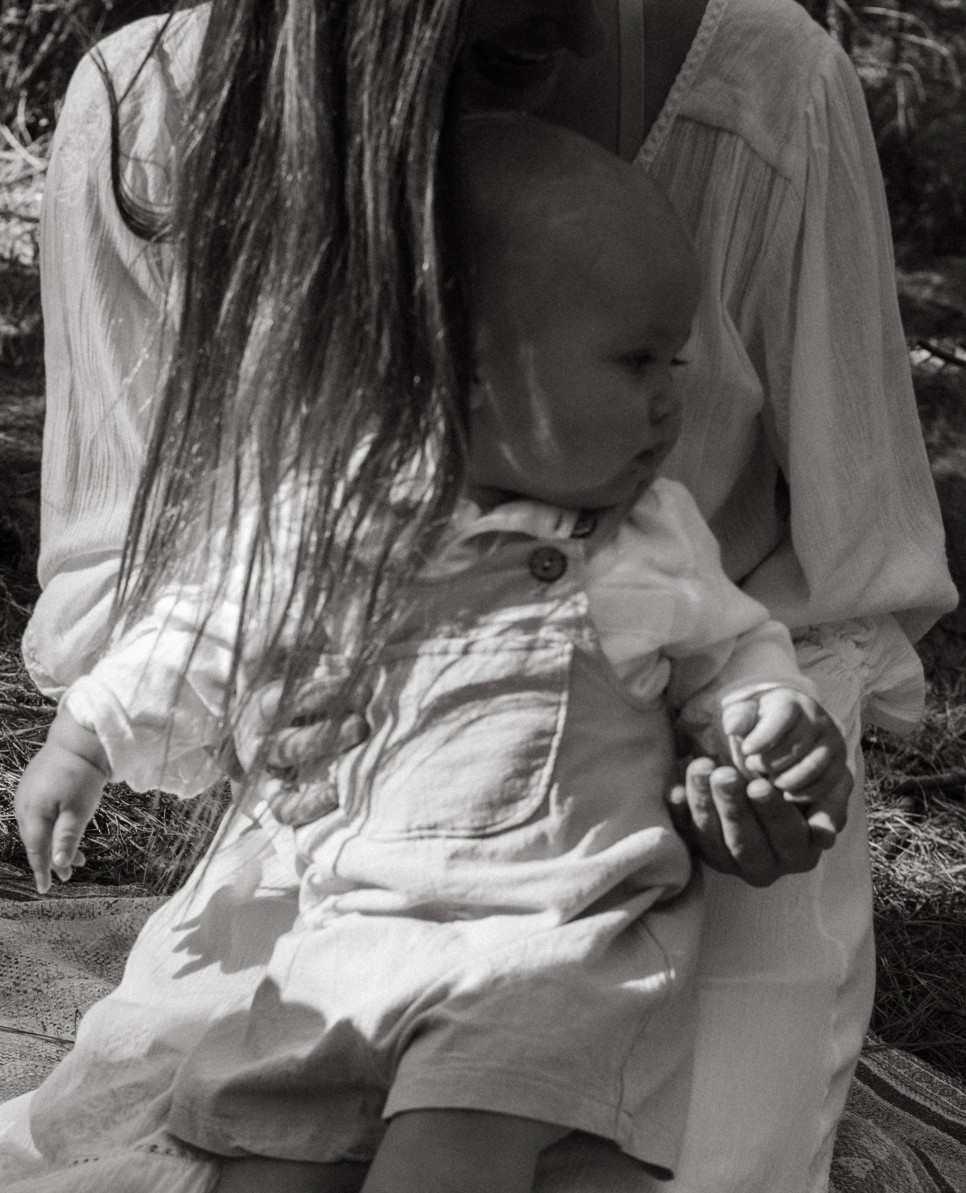 A woman holding a young child on her lap, seated outdoors with grass in the background, in black and white.