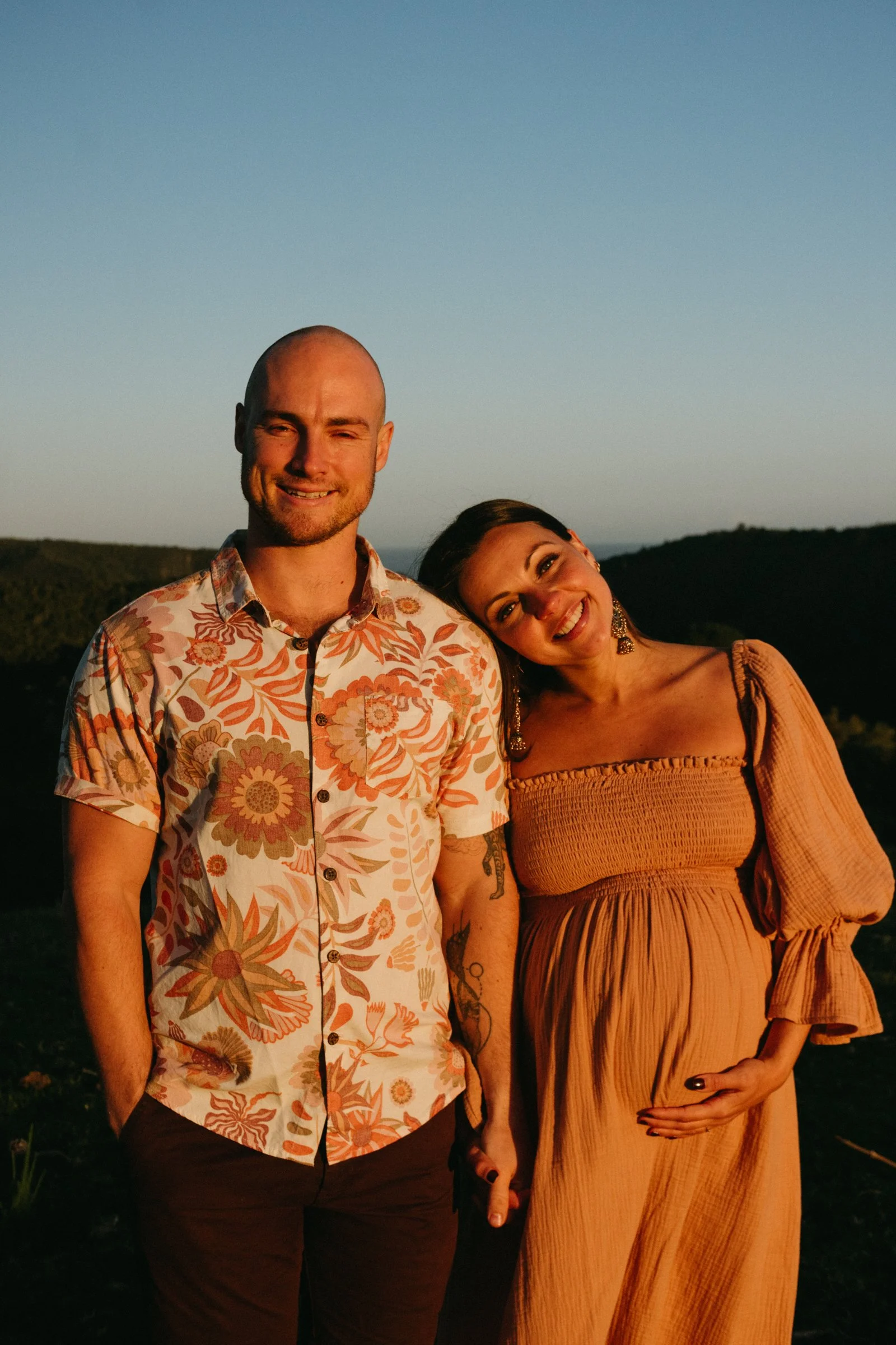 Pregnant woman in a rust dress with her husband facing the camera